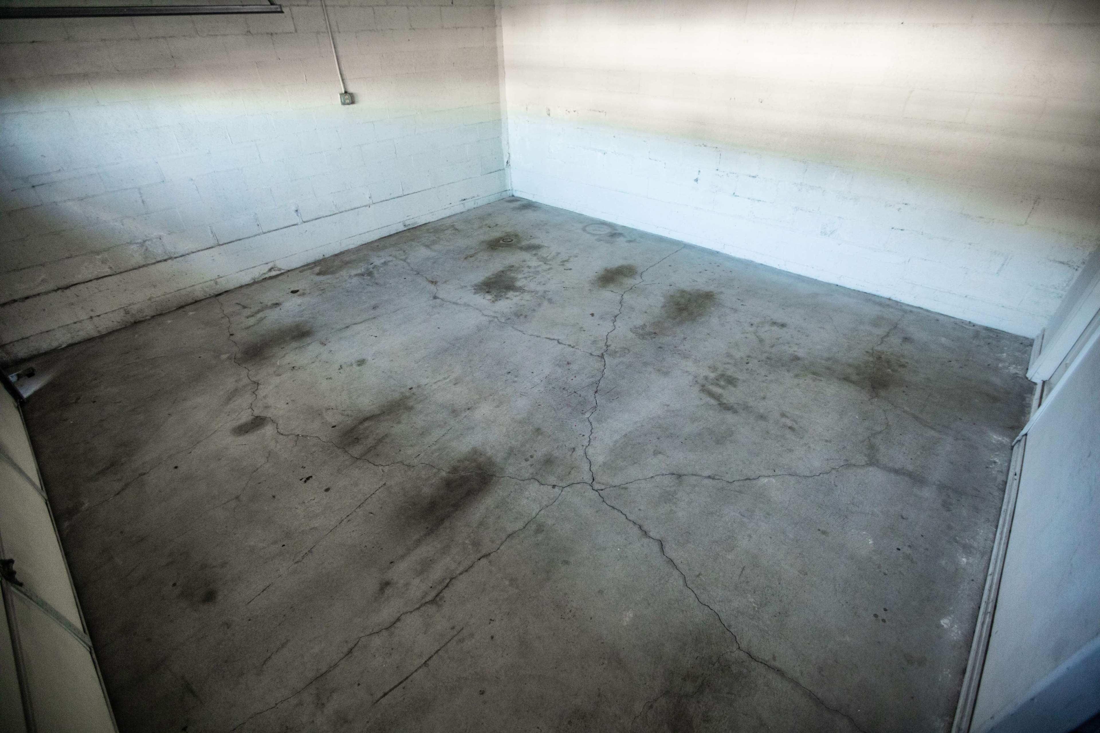 A sparsely furnished room with bare concrete floors and visible cracks.