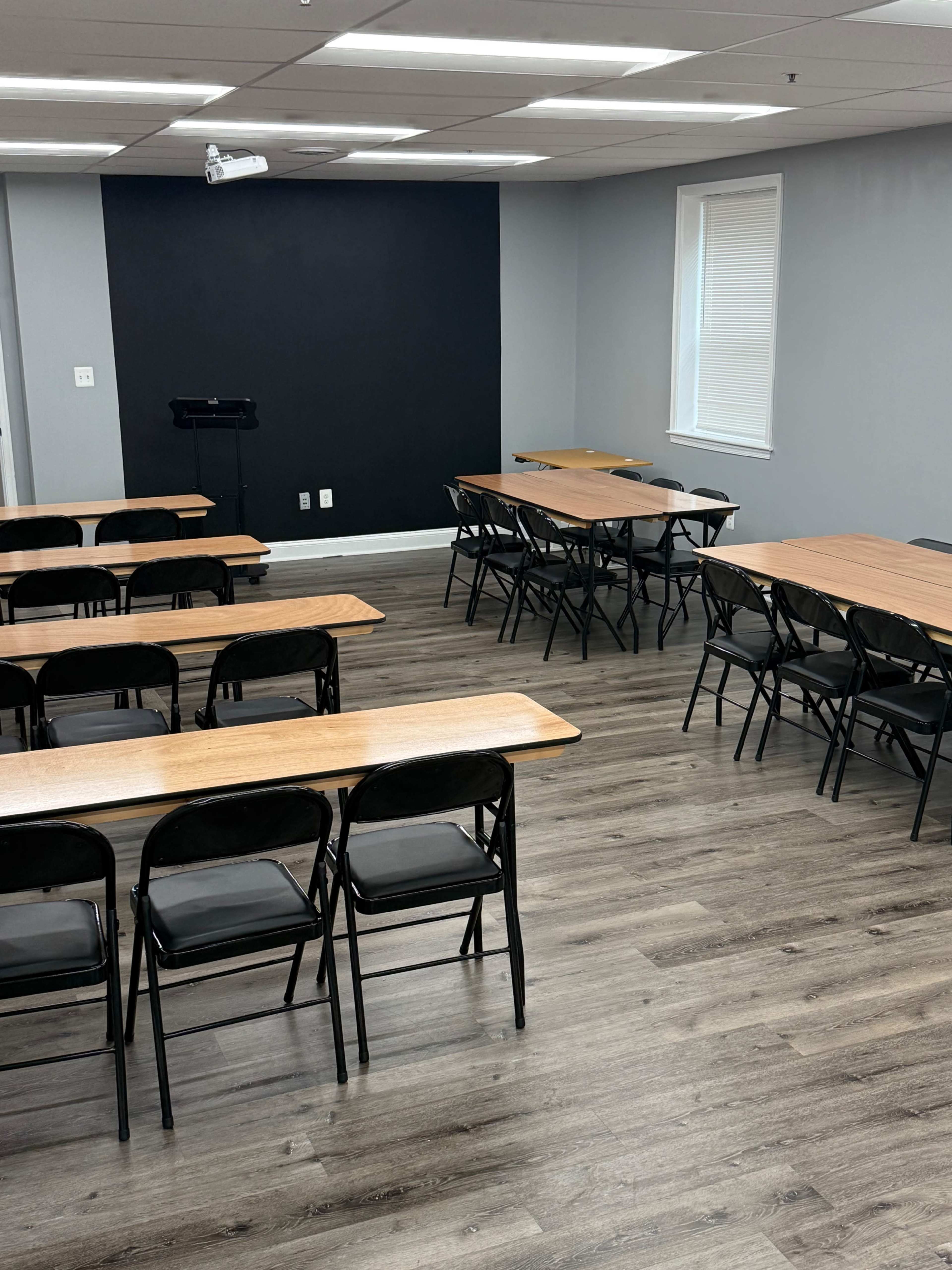The image shows a seminar room with several rows of wooden tables and black folding chairs arranged in a structured seating layout.