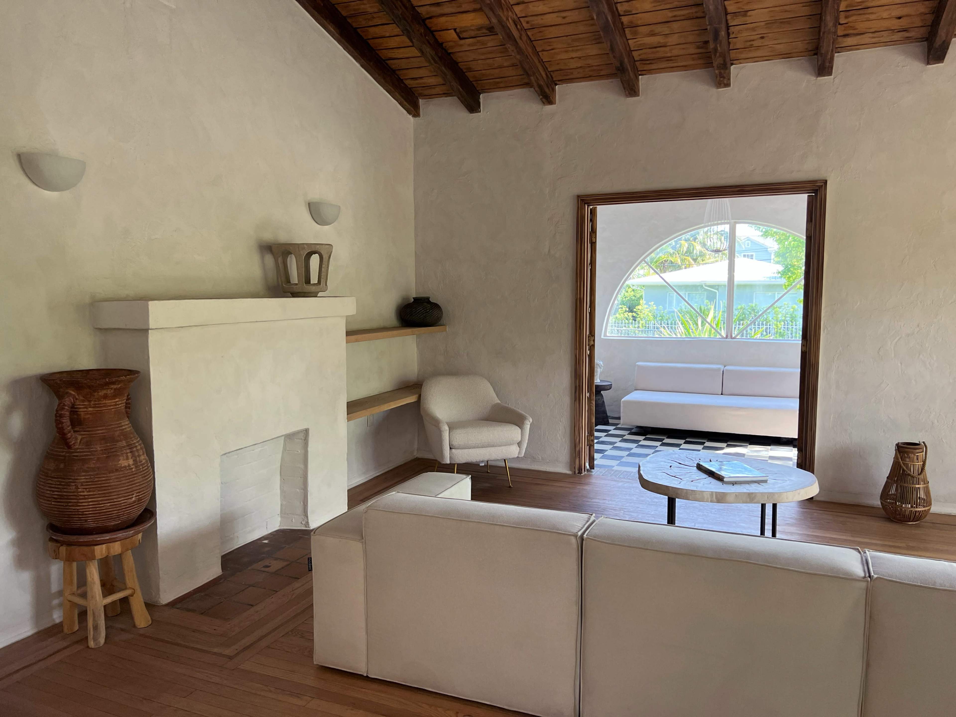 The image shows a living room with a white wall, a wooden ceiling, a sofa, a small table, and a large archway leading to another seating area.