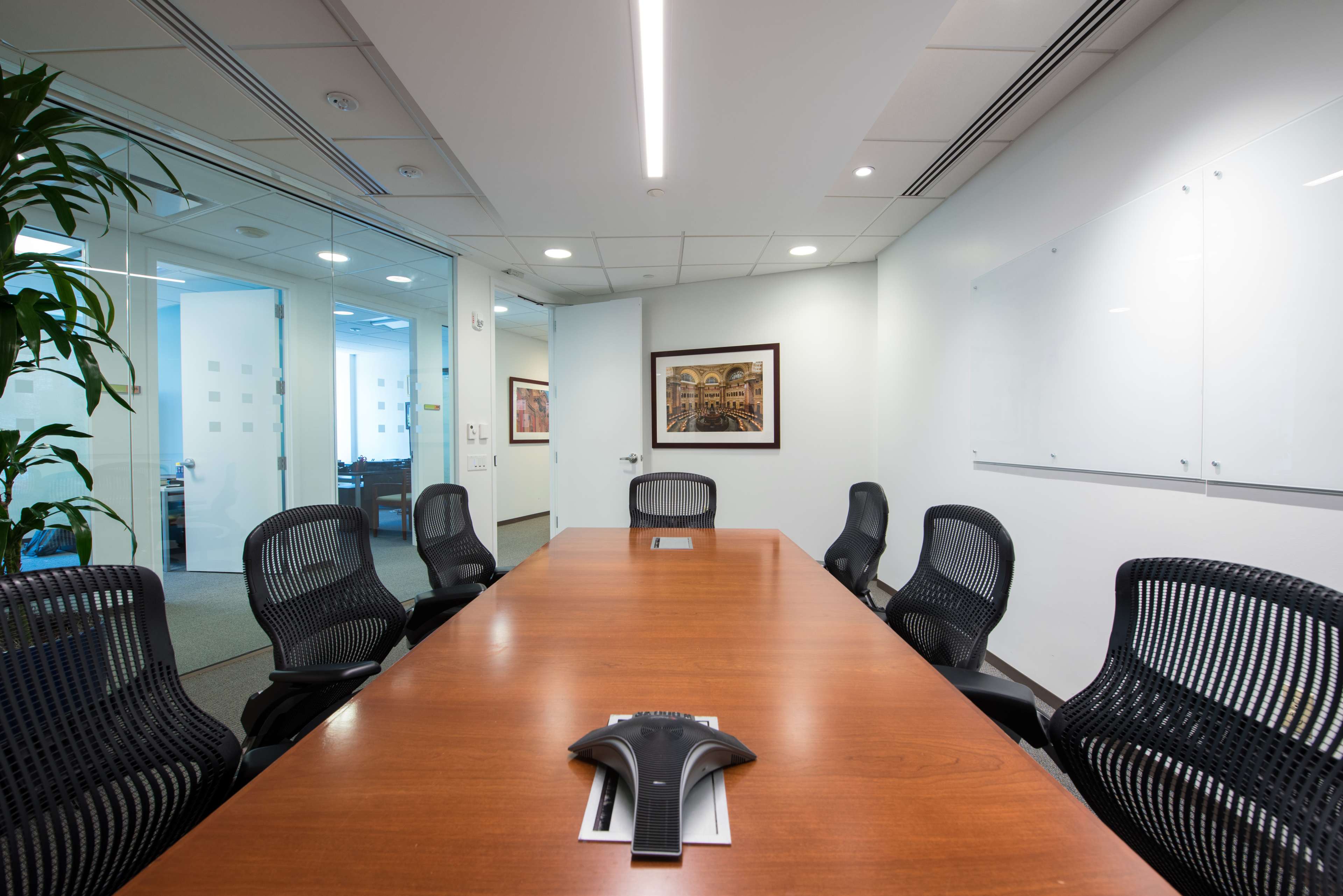 A long wooden conference table is surrounded by black mesh chairs in a well-lit meeting room.