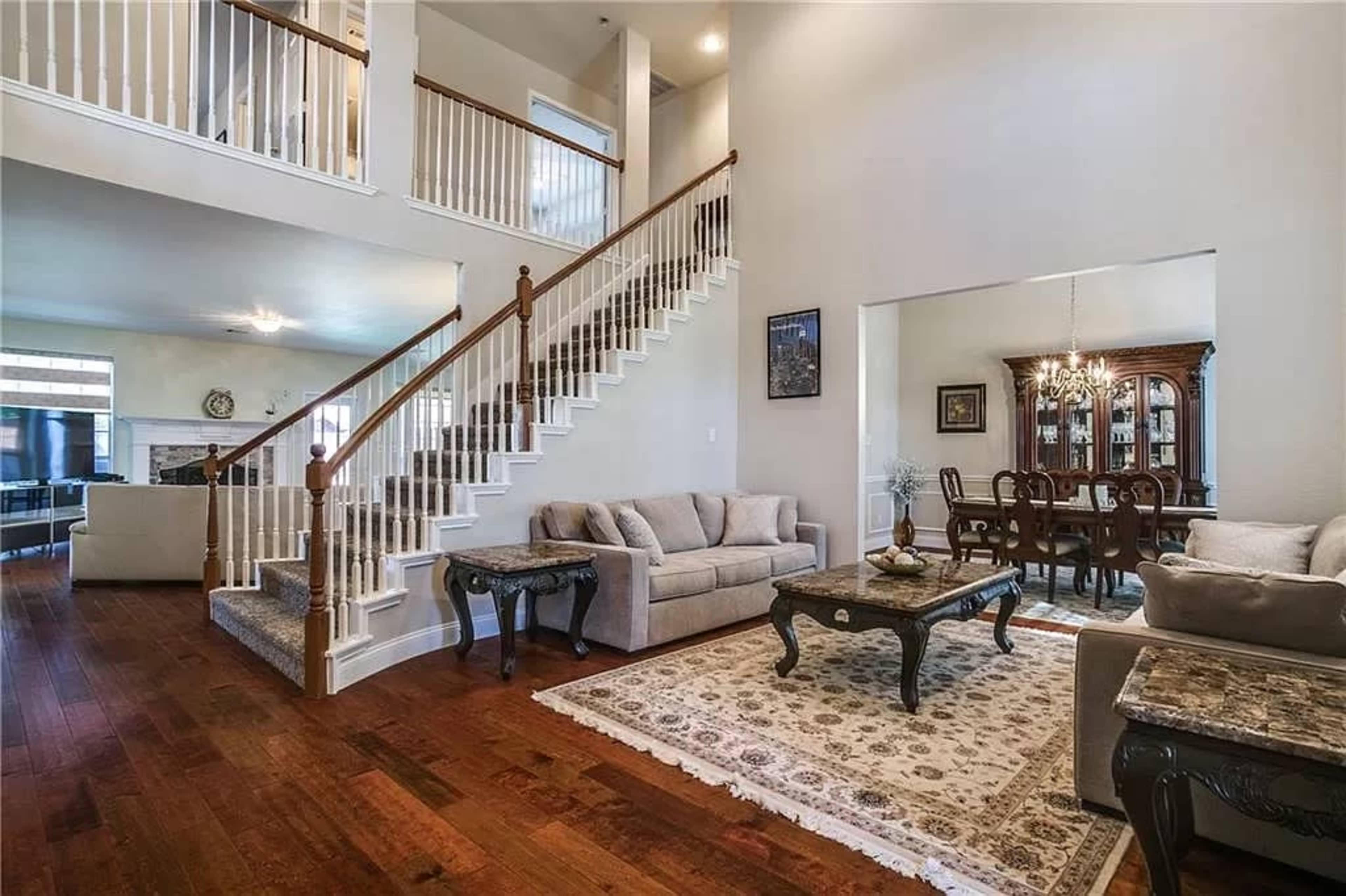 A spacious living room with a staircase, hardwood floors, and a dining area in an adjacent open layout.