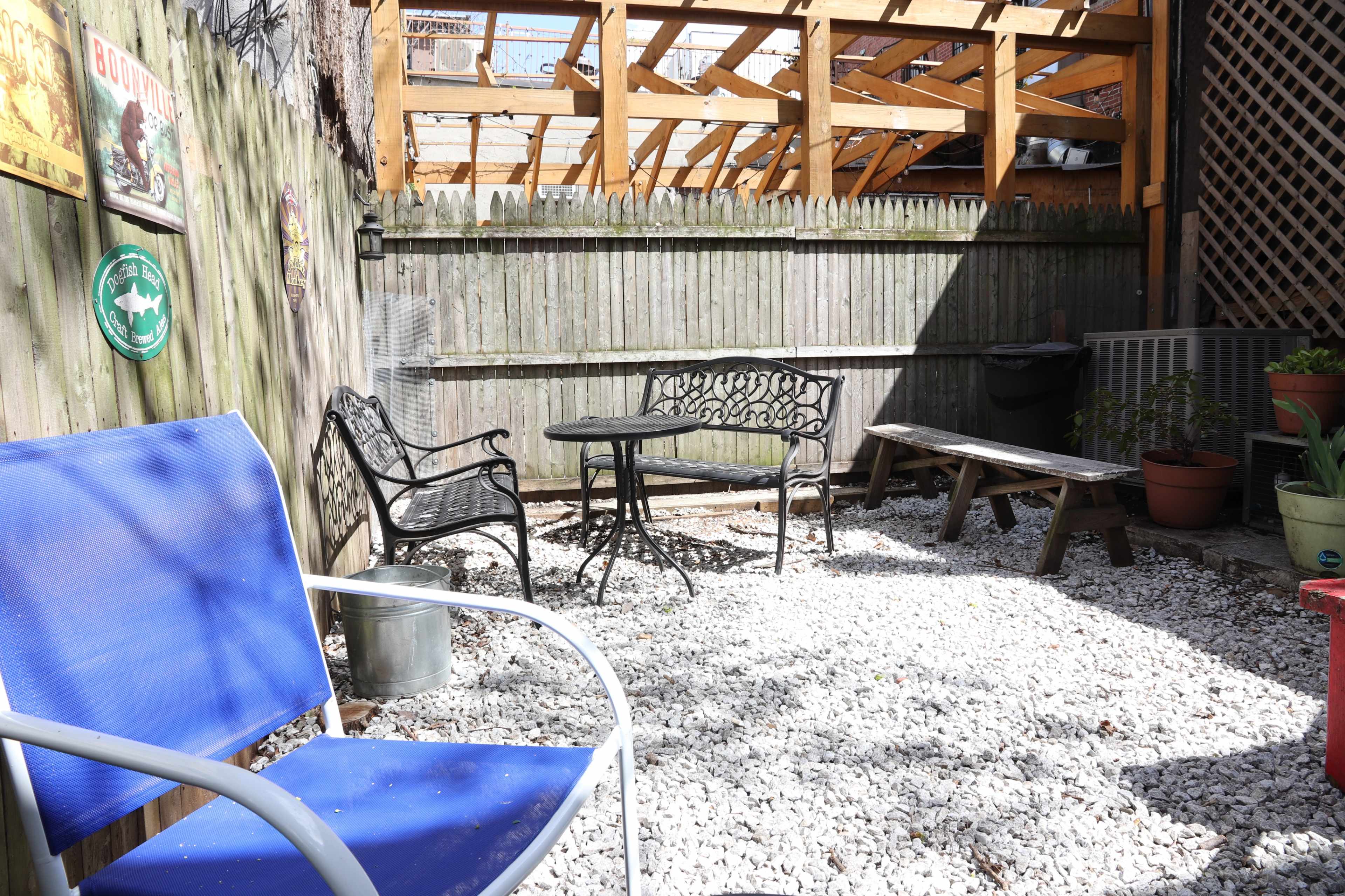 A small outdoor patio area featuring gravel flooring, a metal table with chairs, and various plants in pots.