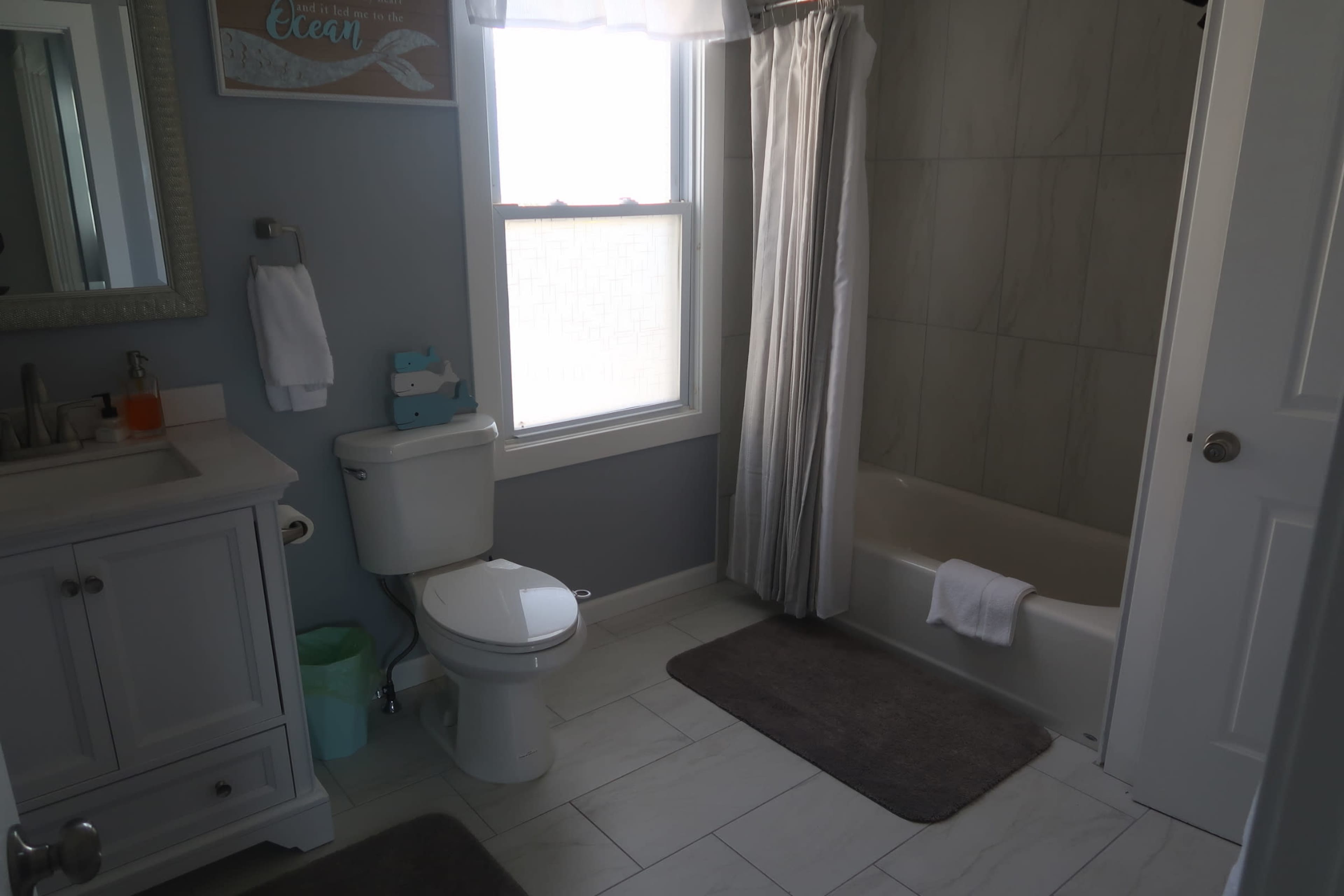 A bathroom featuring a toilet, bathtub with a shower curtain, sink with a mirrored cabinet, and light-colored tiled flooring.