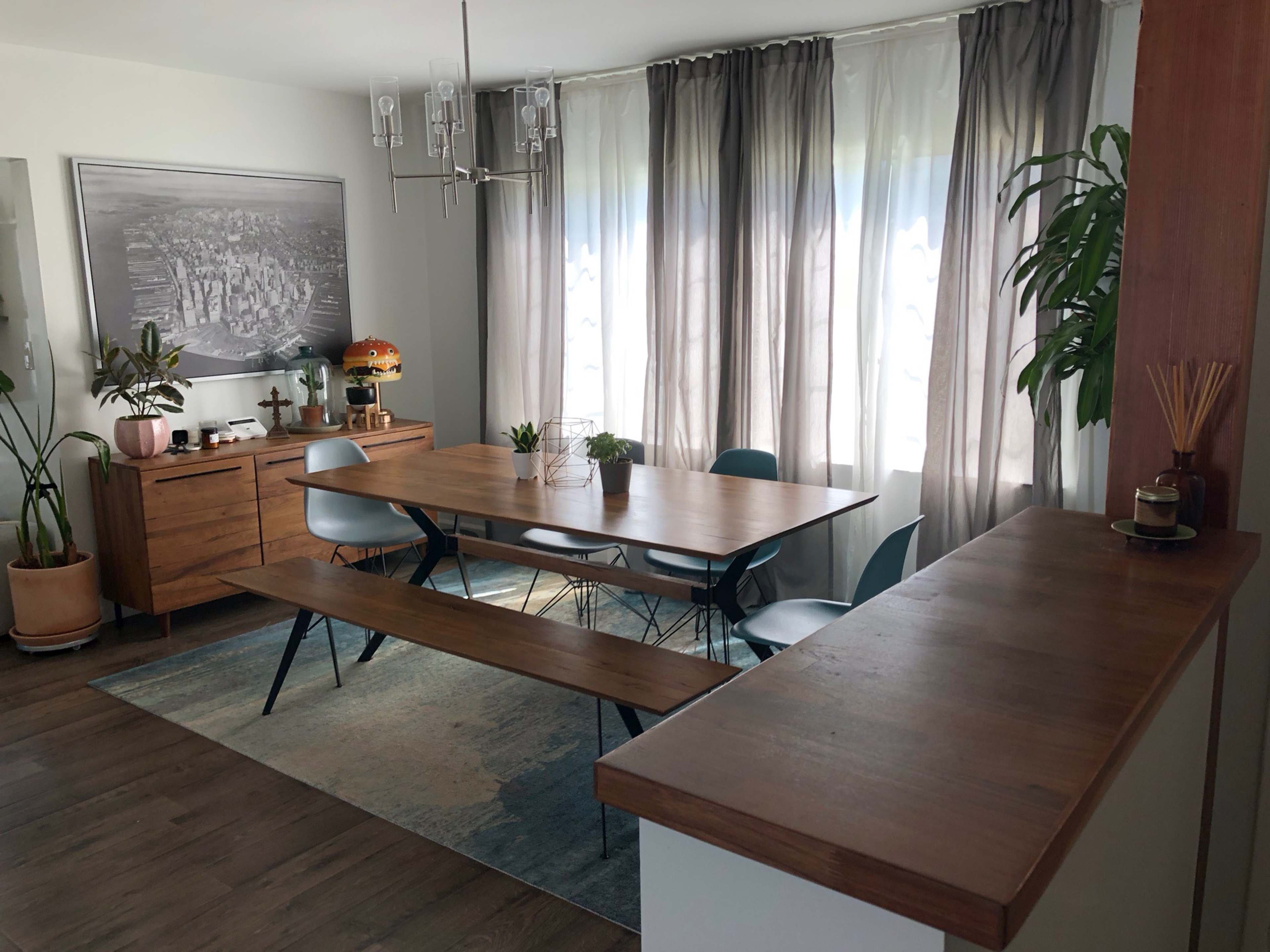 A modern dining area with a wooden table, bench seating, chairs, and large windows dressed with sheer curtains.