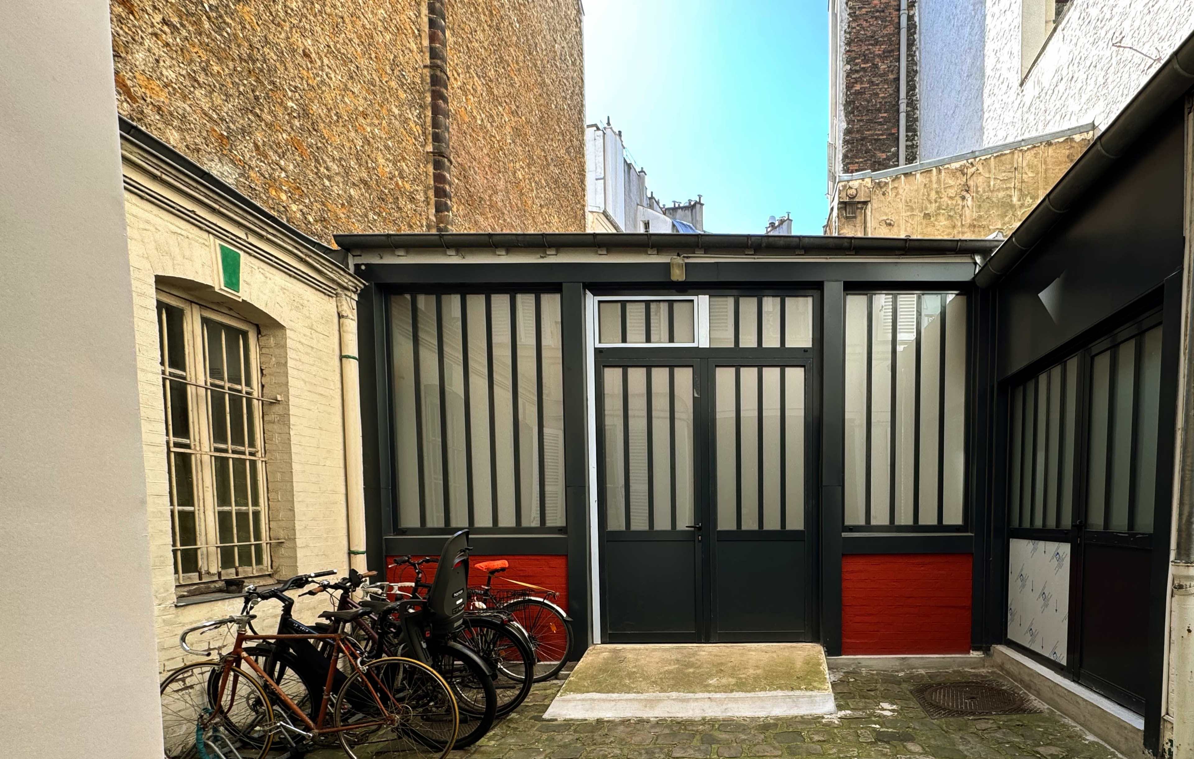 The image shows a courtyard with a glass-paneled building at the center and several bicycles parked in front.