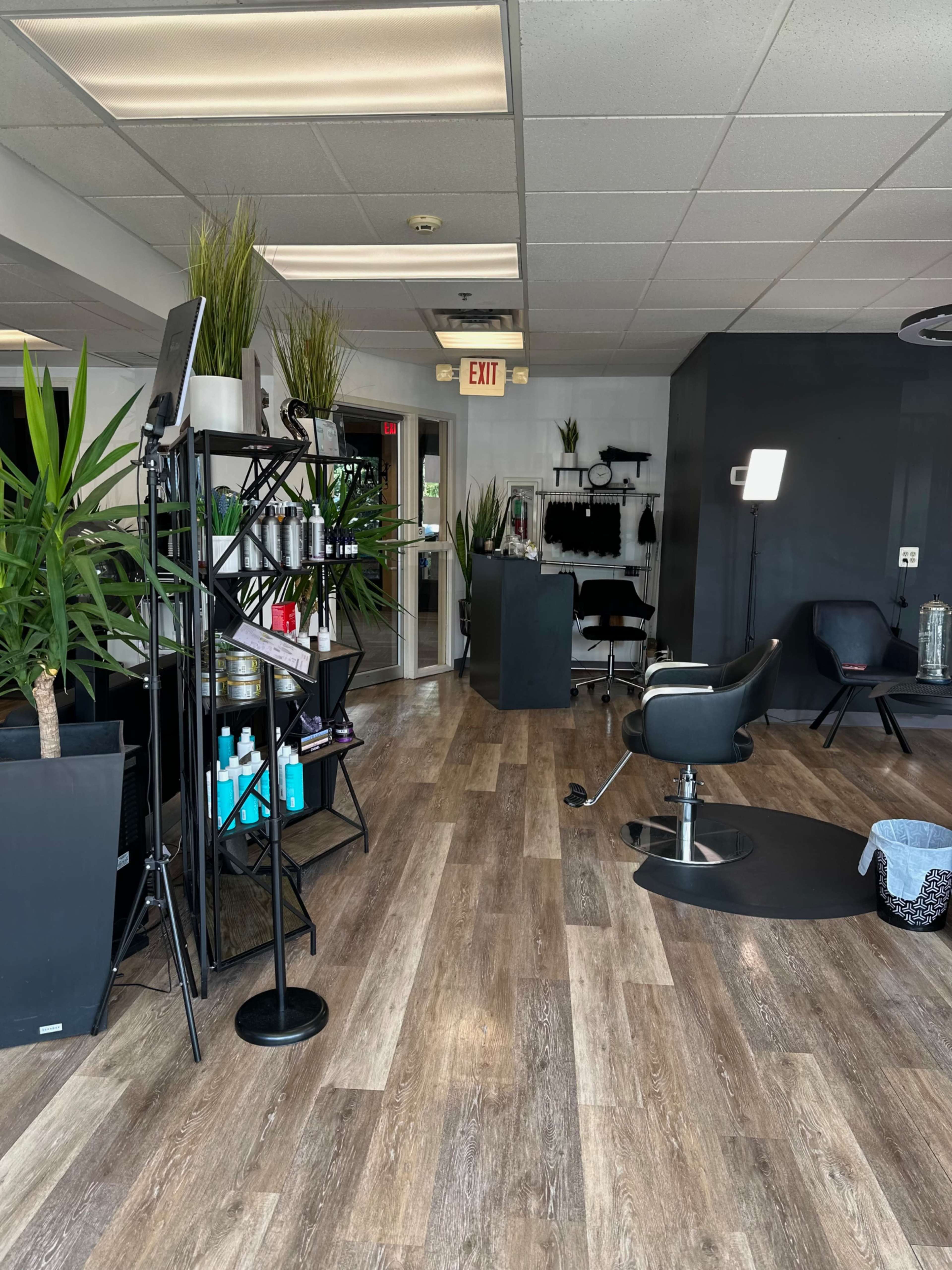 A modern hair salon with chairs, a styling station, and indoor plants arranged around a wooden floor.