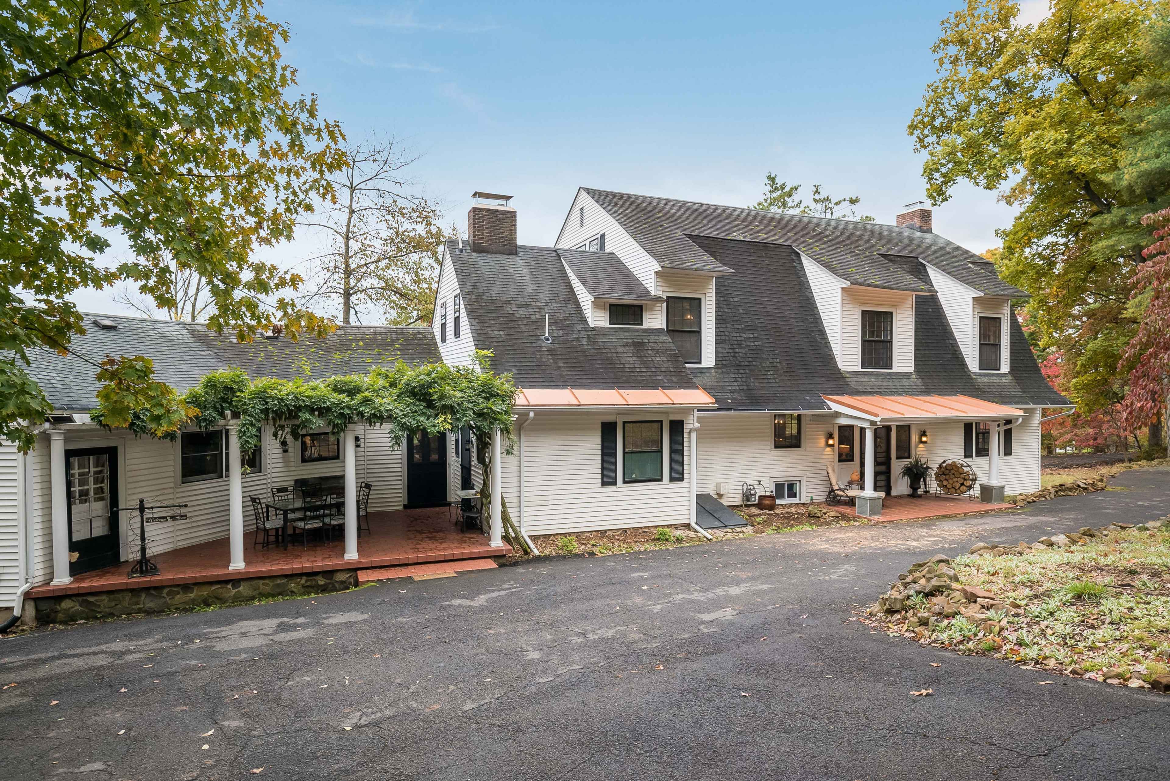 A white, multi-level house with a front porch surrounded by trees and a paved driveway.