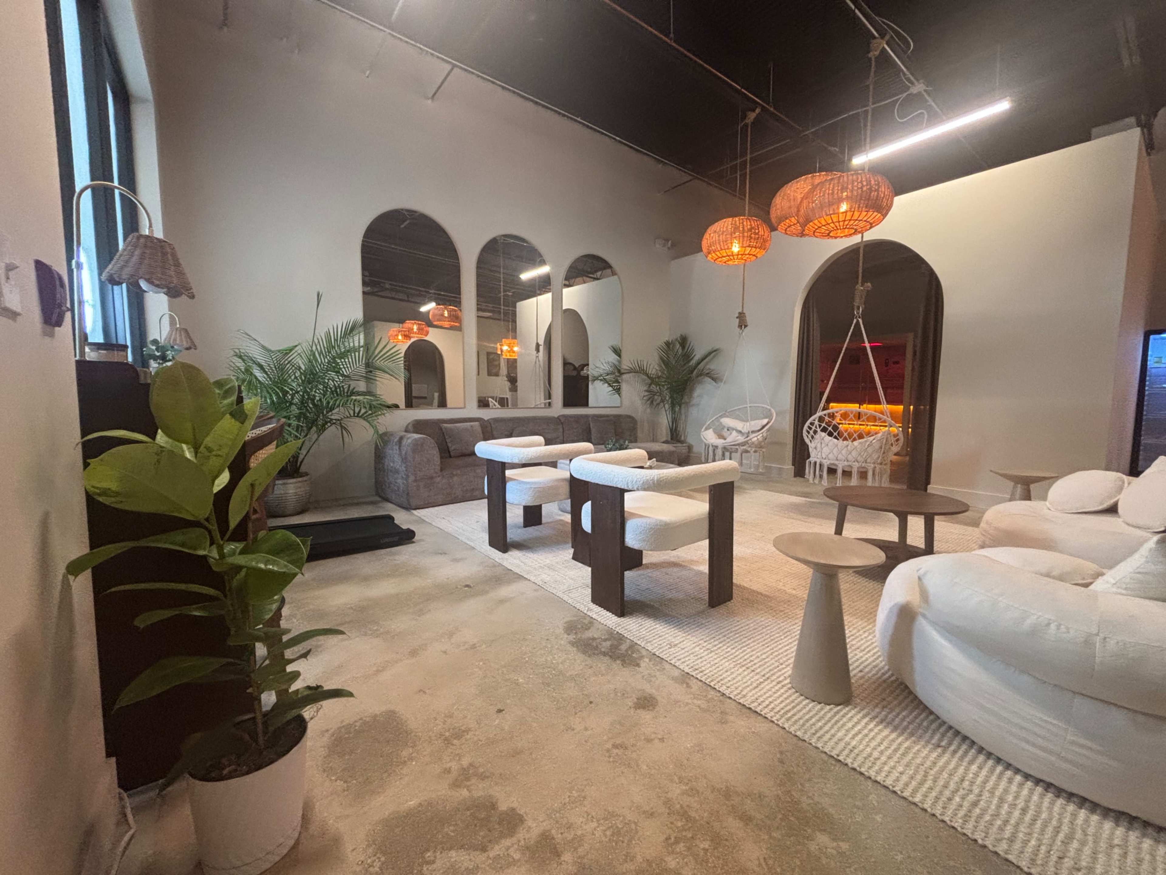 The image shows a modern, airy interior space featuring several seating areas with minimalist furniture and decorative plants.