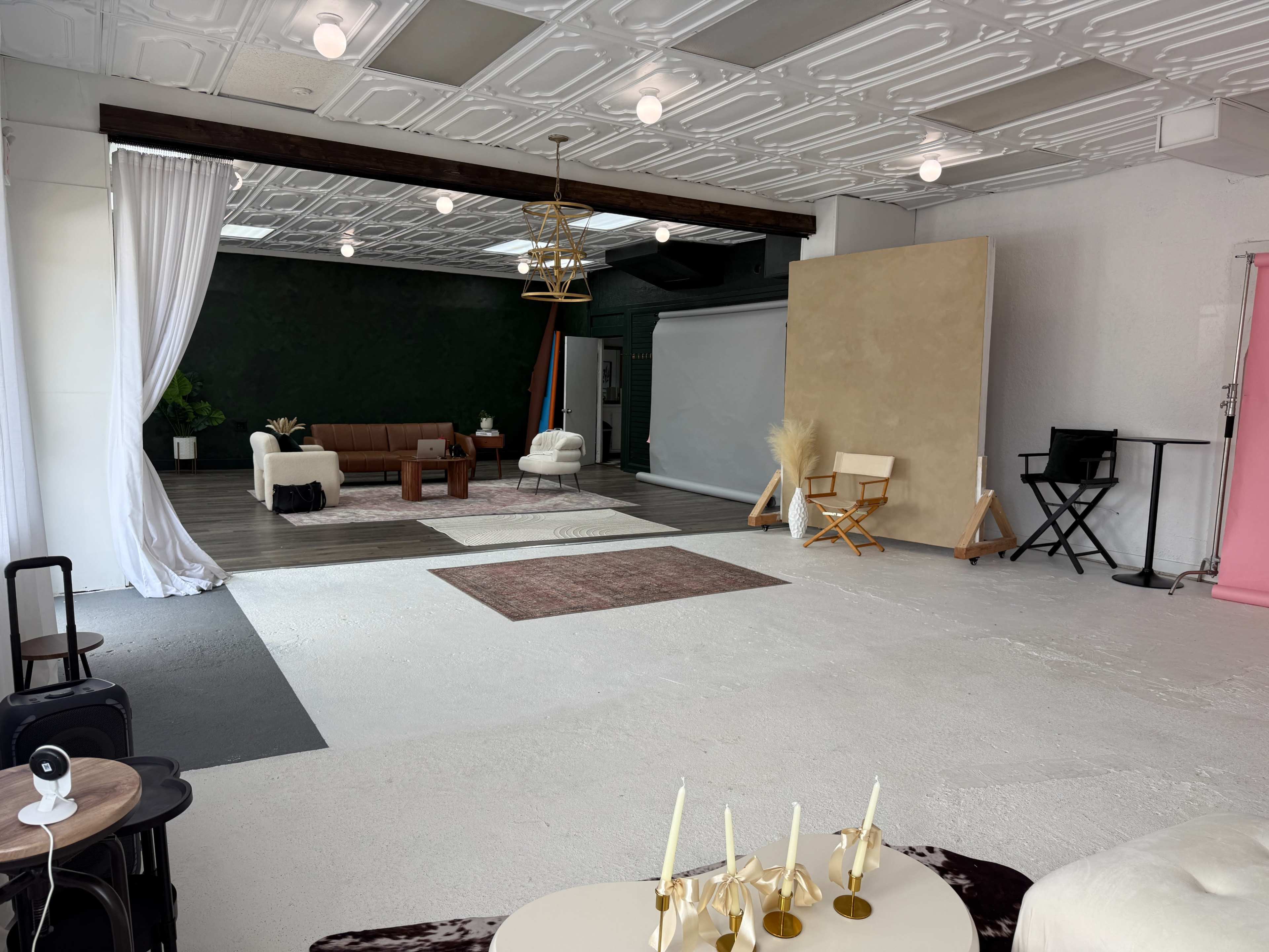 The image shows a spacious photo studio featuring a variety of seating arrangements, a large backdrop, and distinct zones for different setups.