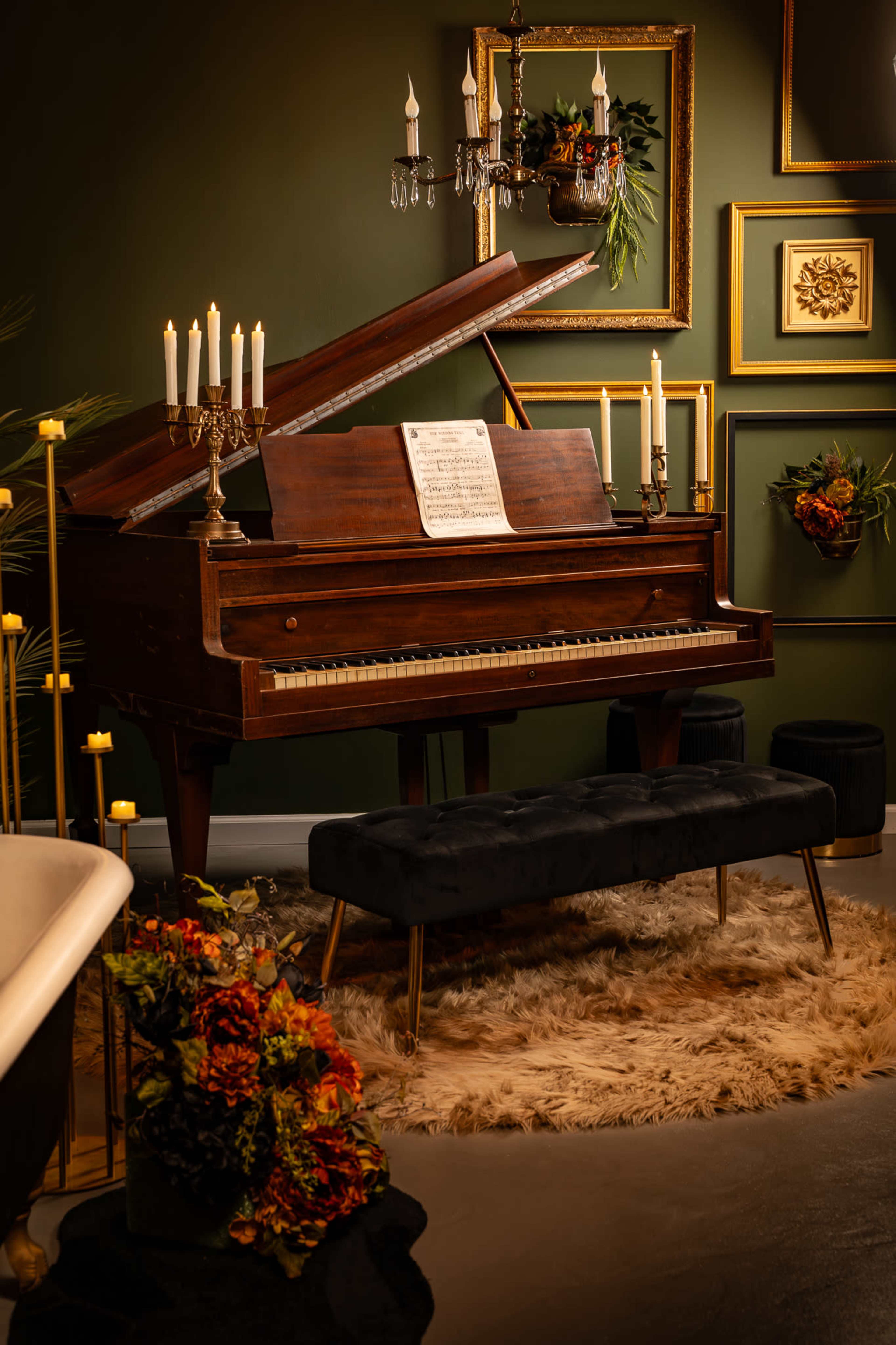 A grand piano with sheet music sits beside a velvet bench in a warmly decorated room featuring floral arrangements and framed art.