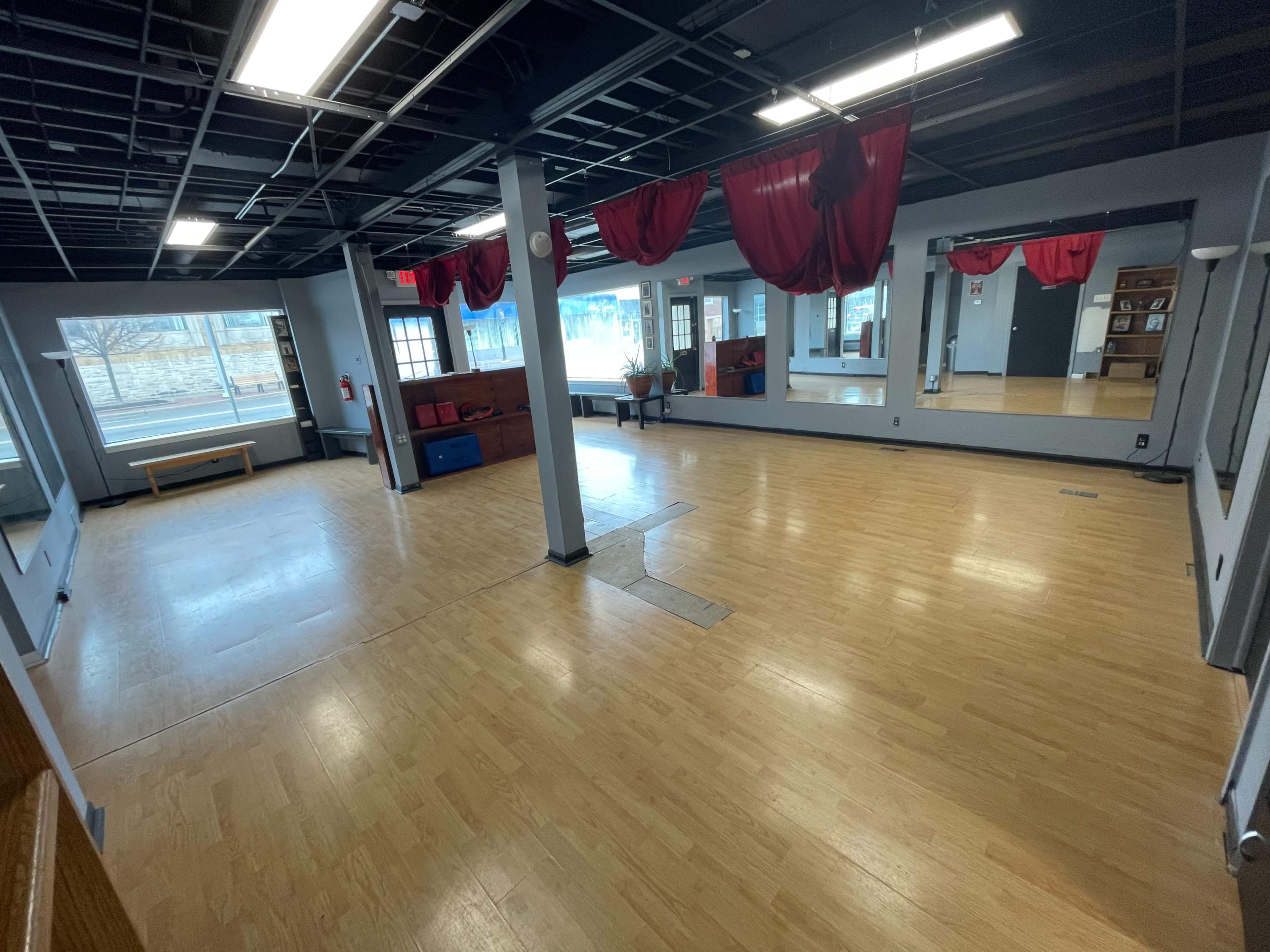 A spacious, empty studio with wooden floors, large mirrors, and red drapes hanging from the ceiling.