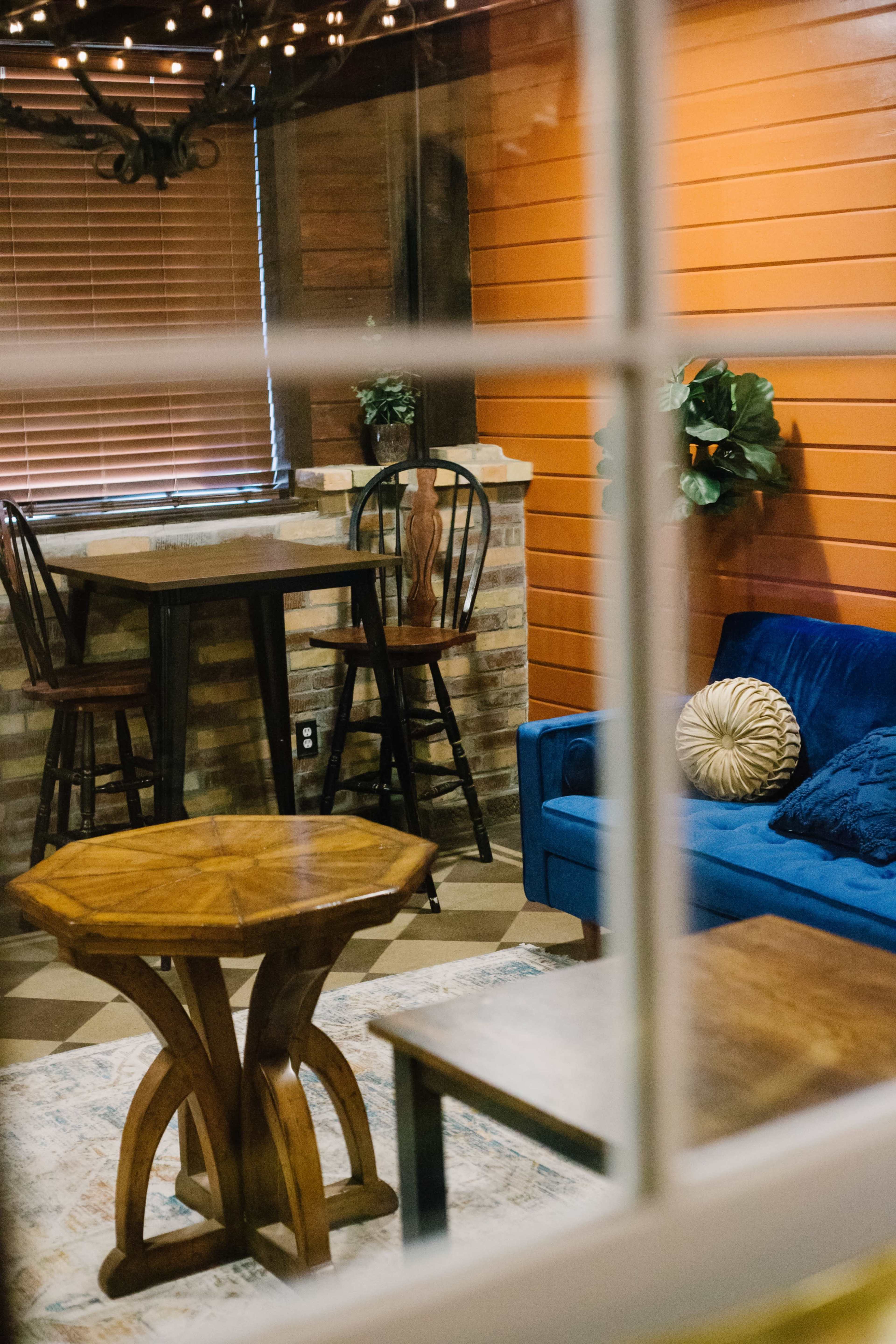 A well-furnished room with a blue sofa, a wooden table, and barstools near a brick feature wall, all visible through a window.