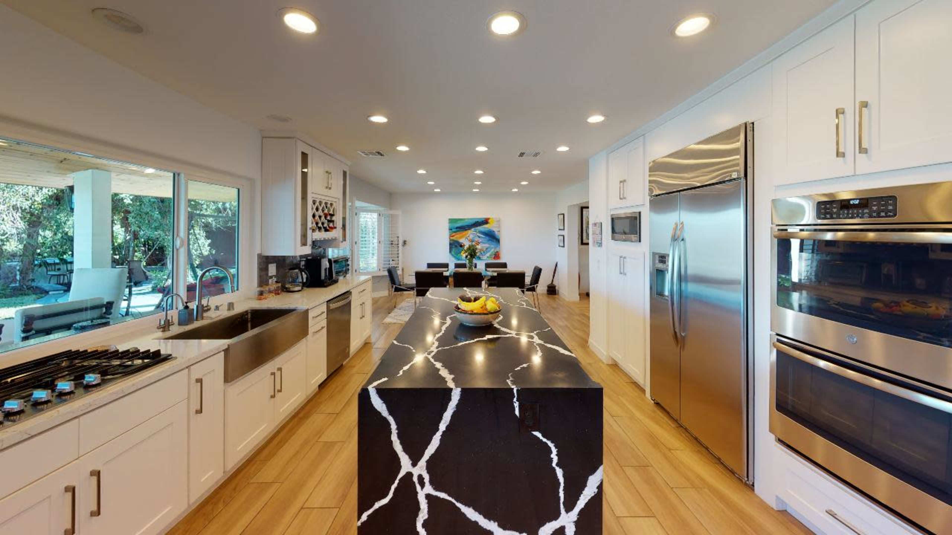 A modern kitchen features an island with a black and white marble countertop, stainless steel appliances, and white cabinetry.