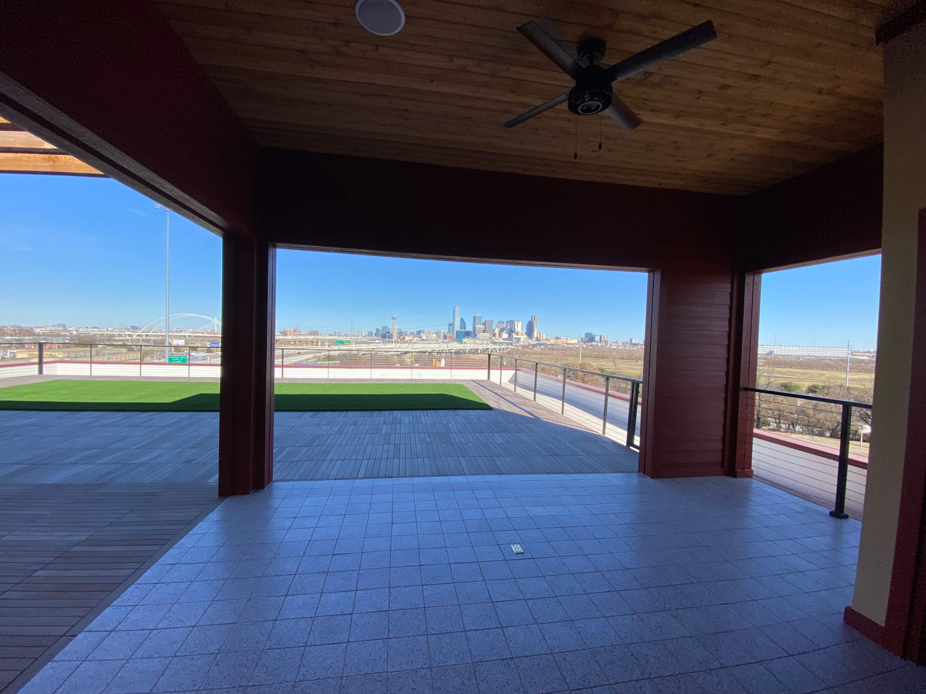 The image shows an open interior space with a ceiling fan, leading to a view of a city skyline through large windows.