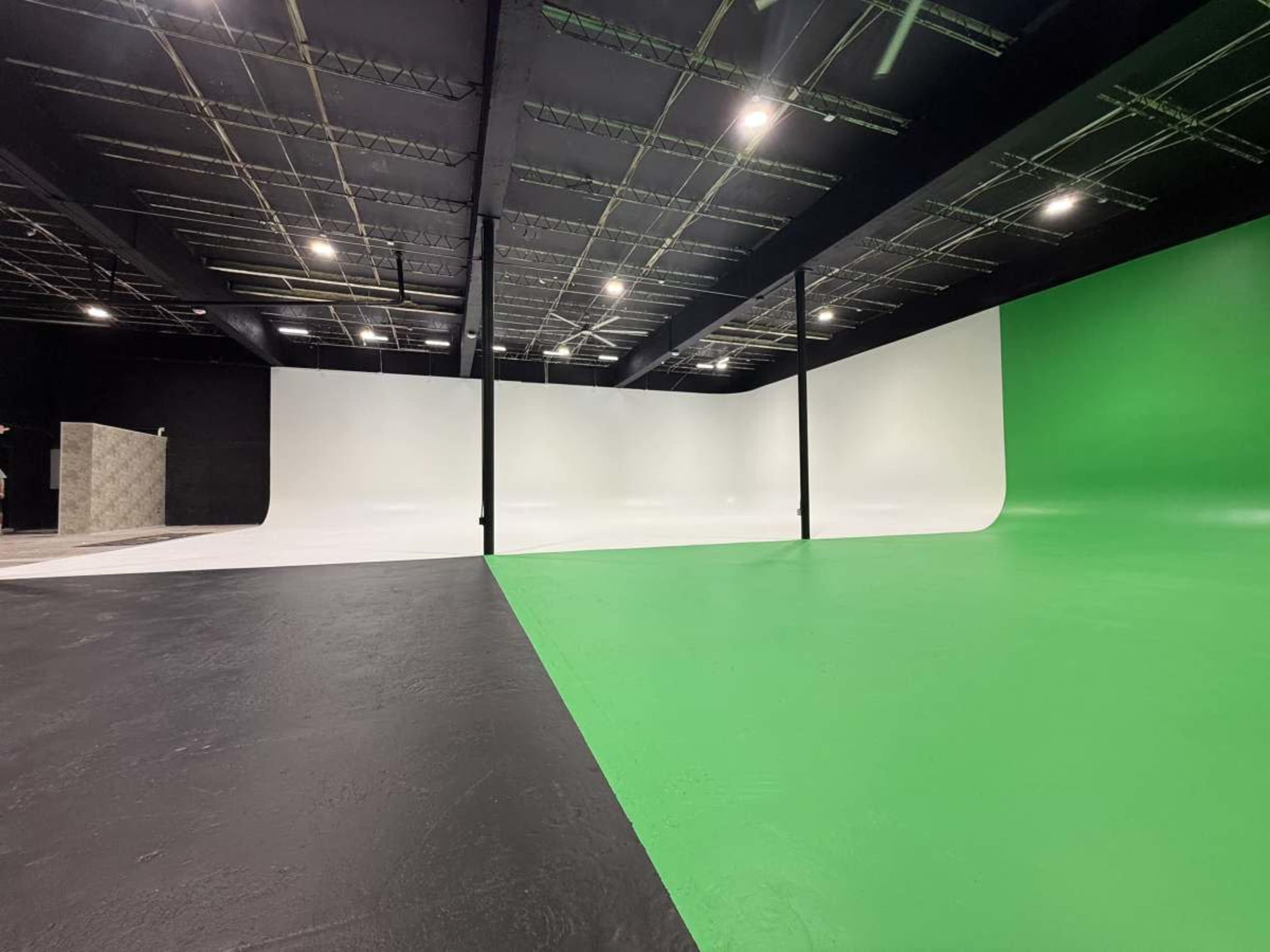 The image shows a spacious studio with a black floor and a large white backdrop on one side, transitioning to a green backdrop on the other side.