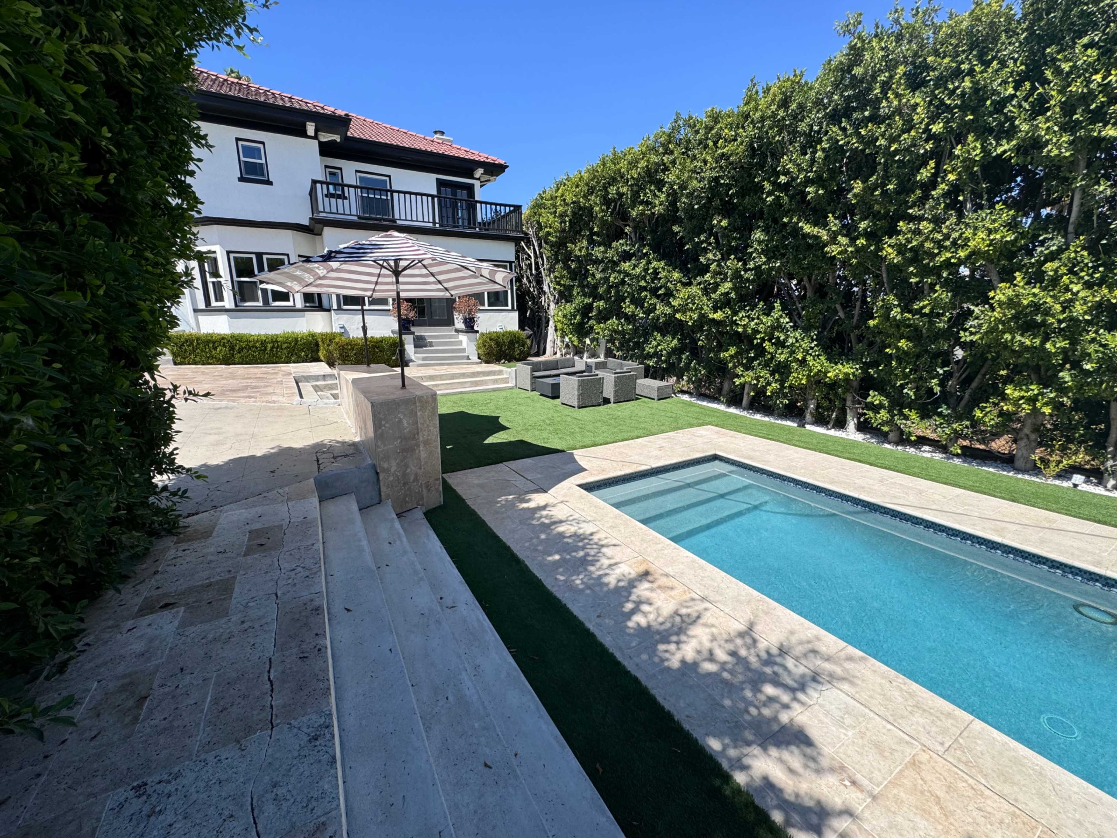 A well-maintained backyard features a swimming pool, patio seating, and manicured greenery surrounding a two-story house.