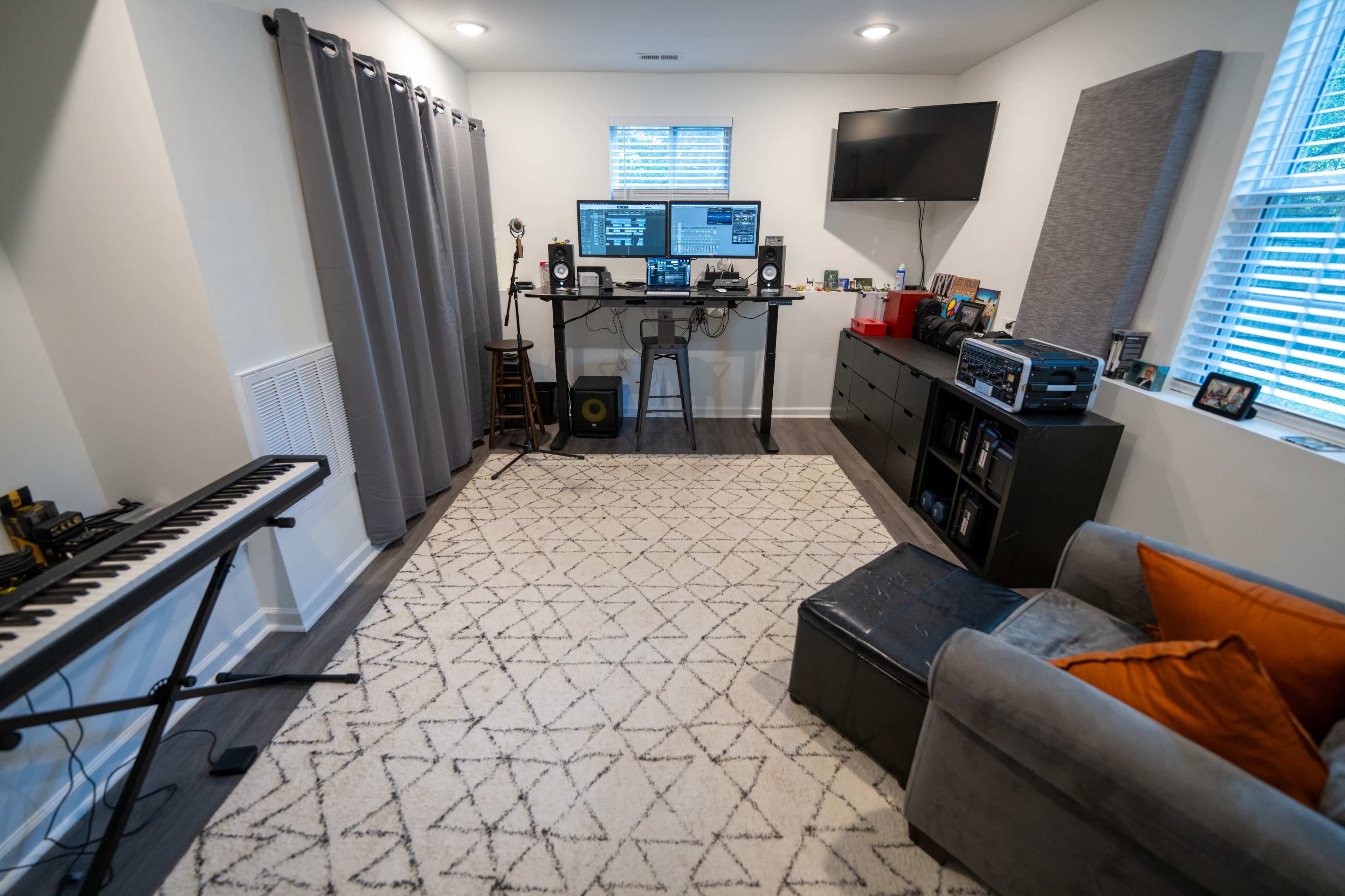 The image shows a home studio setup with a computer desk, sound equipment, a keyboard, and a gray couch on a patterned rug.