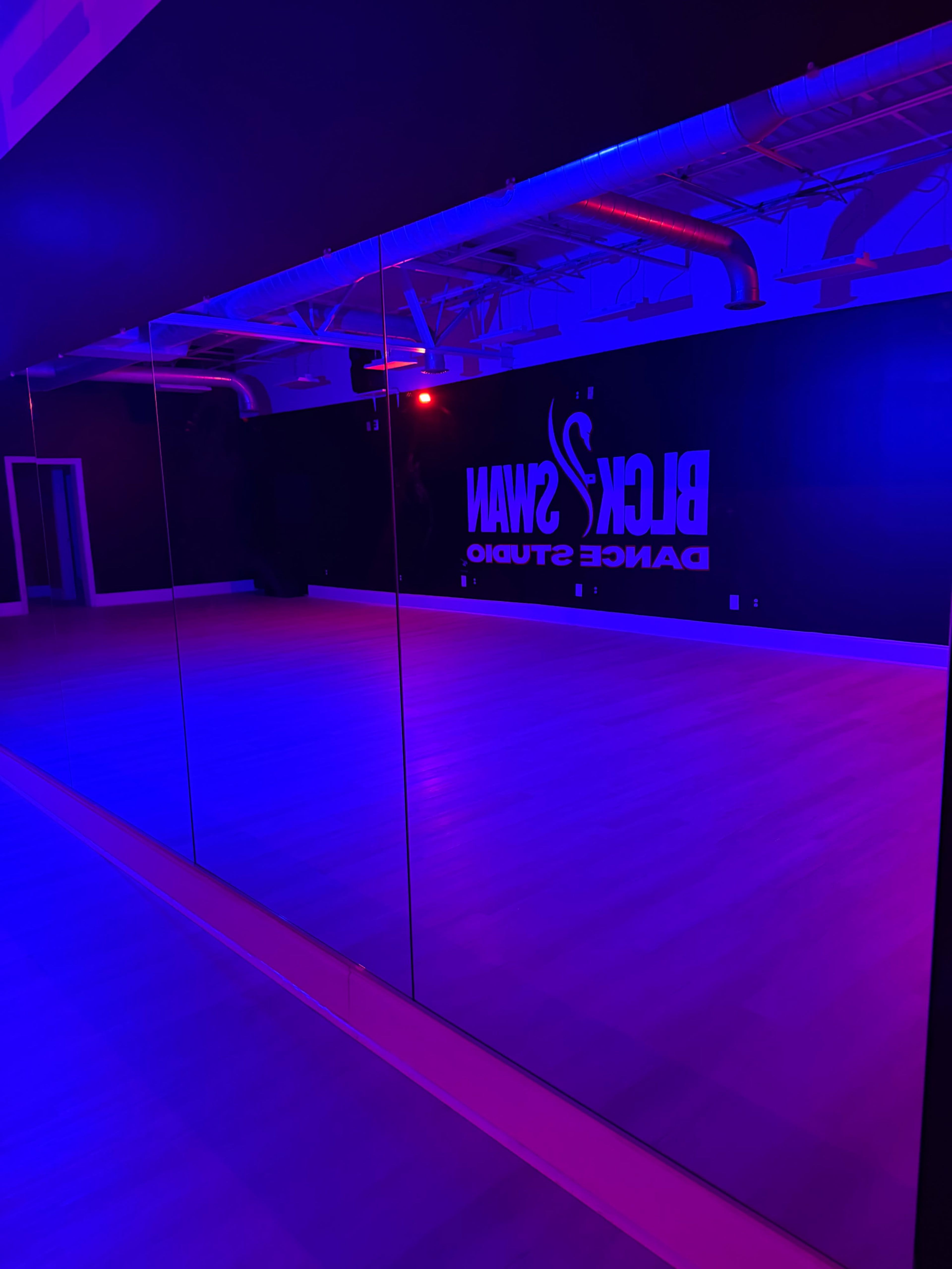 The image shows a dance studio with purple lighting and a mirrored wall reflecting the studio's branding.