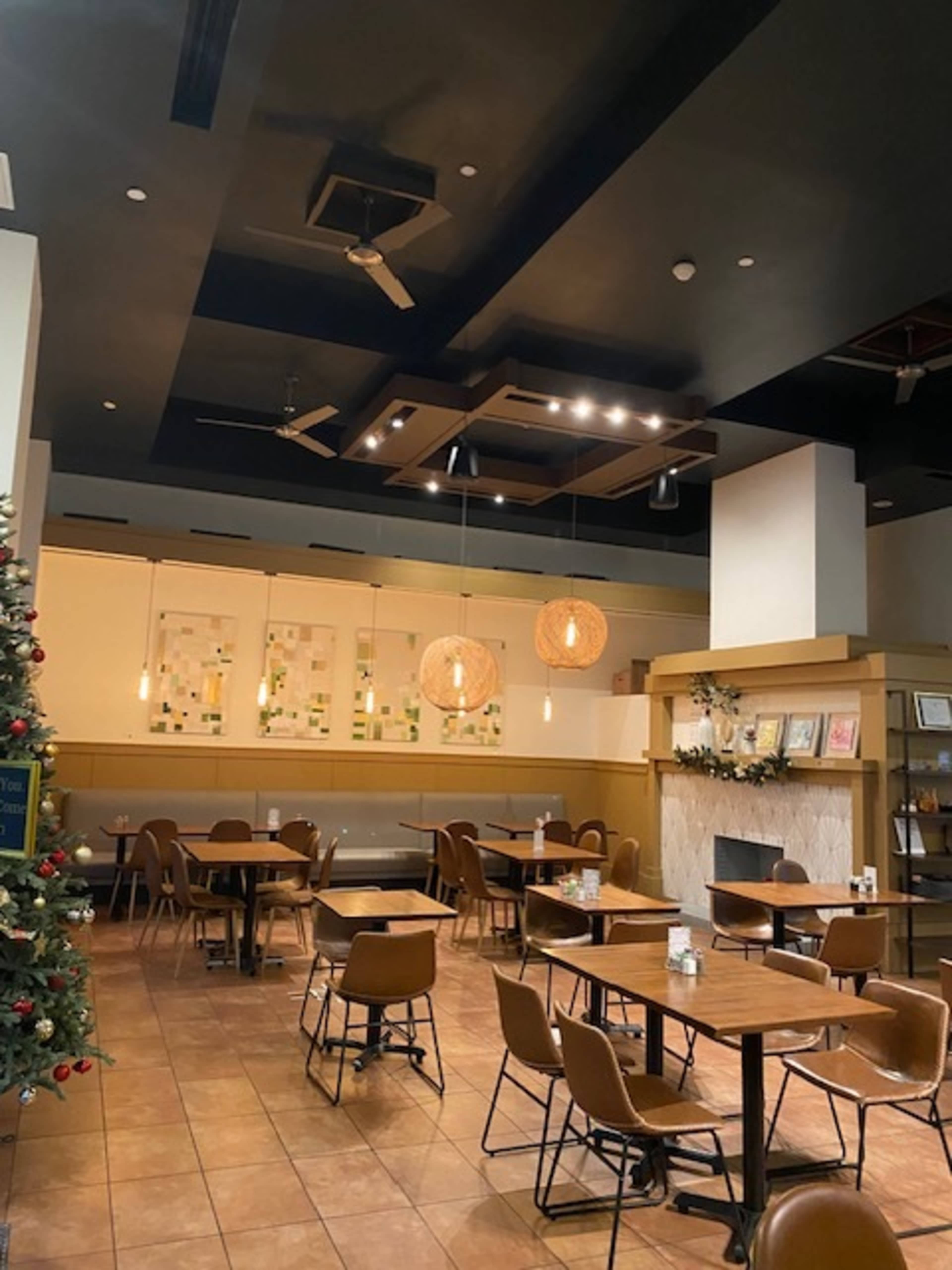 The image shows an empty café with wooden tables and chairs, illuminated by pendant lights and featuring a decorative Christmas tree in the corner.