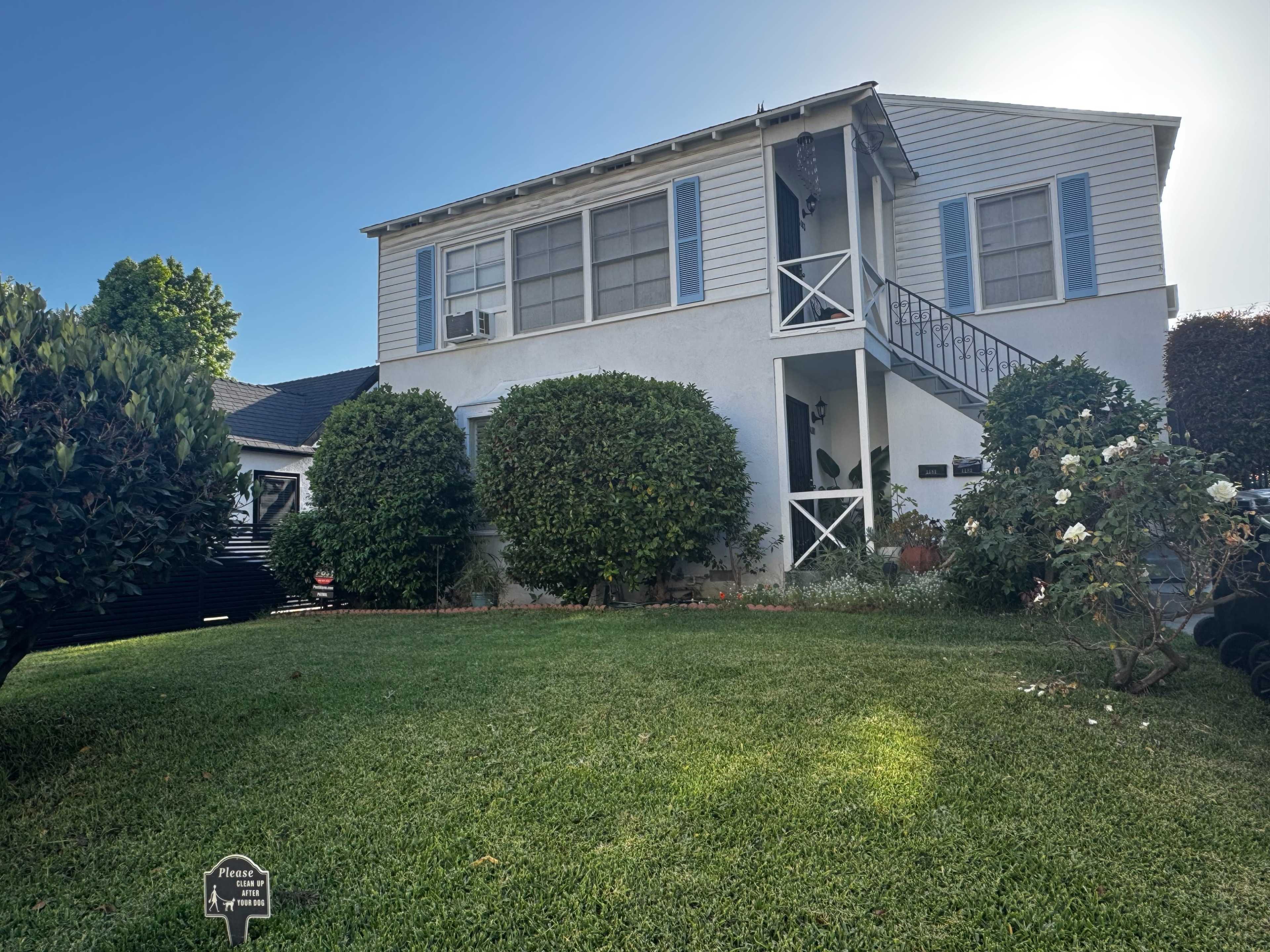 A two-story house with a light blue exterior and a front staircase is surrounded by well-maintained greenery and lawn.