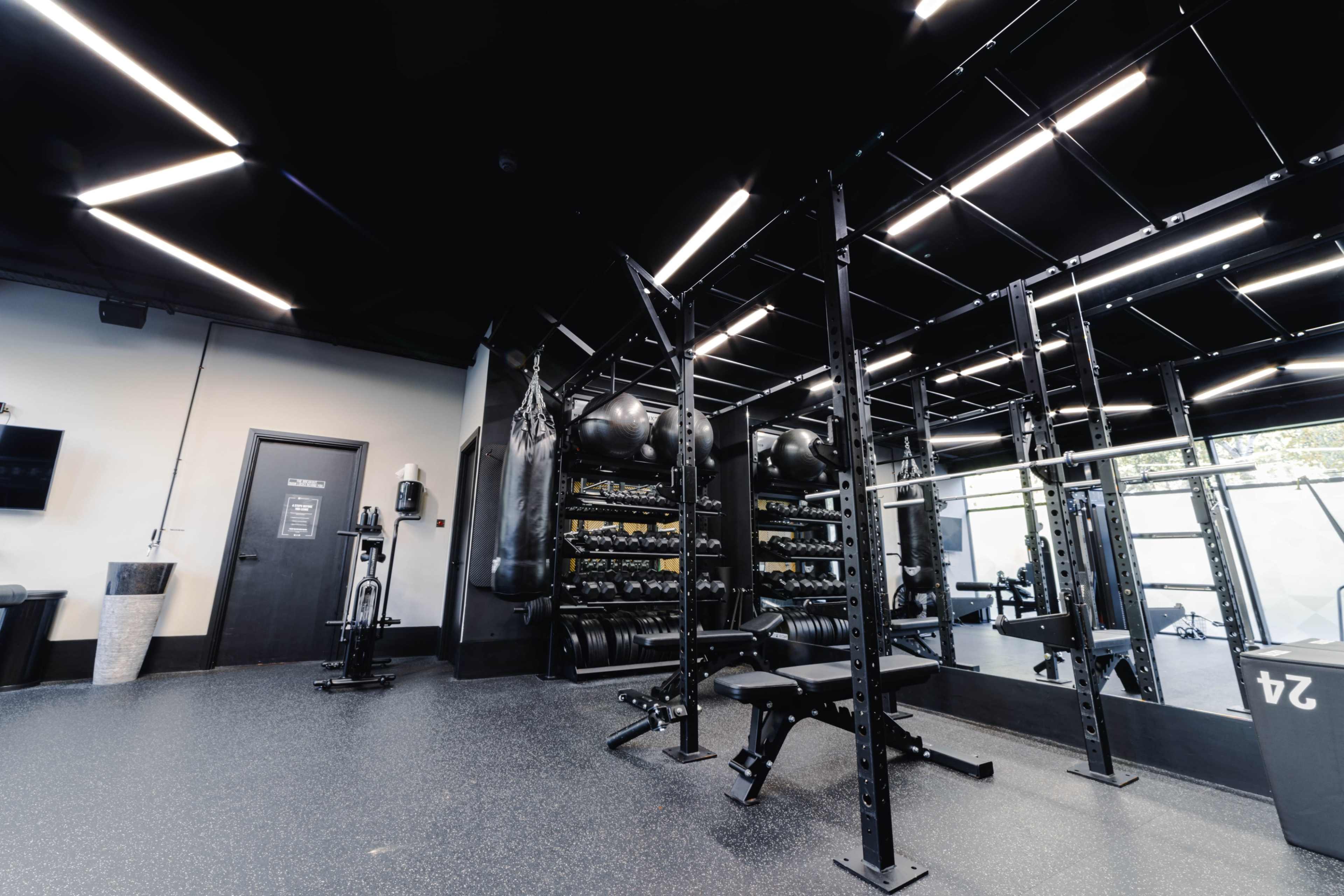 The image shows a modern gym interior featuring weightlifting equipment, a squat rack, and a mirrored wall in a well-lit space.