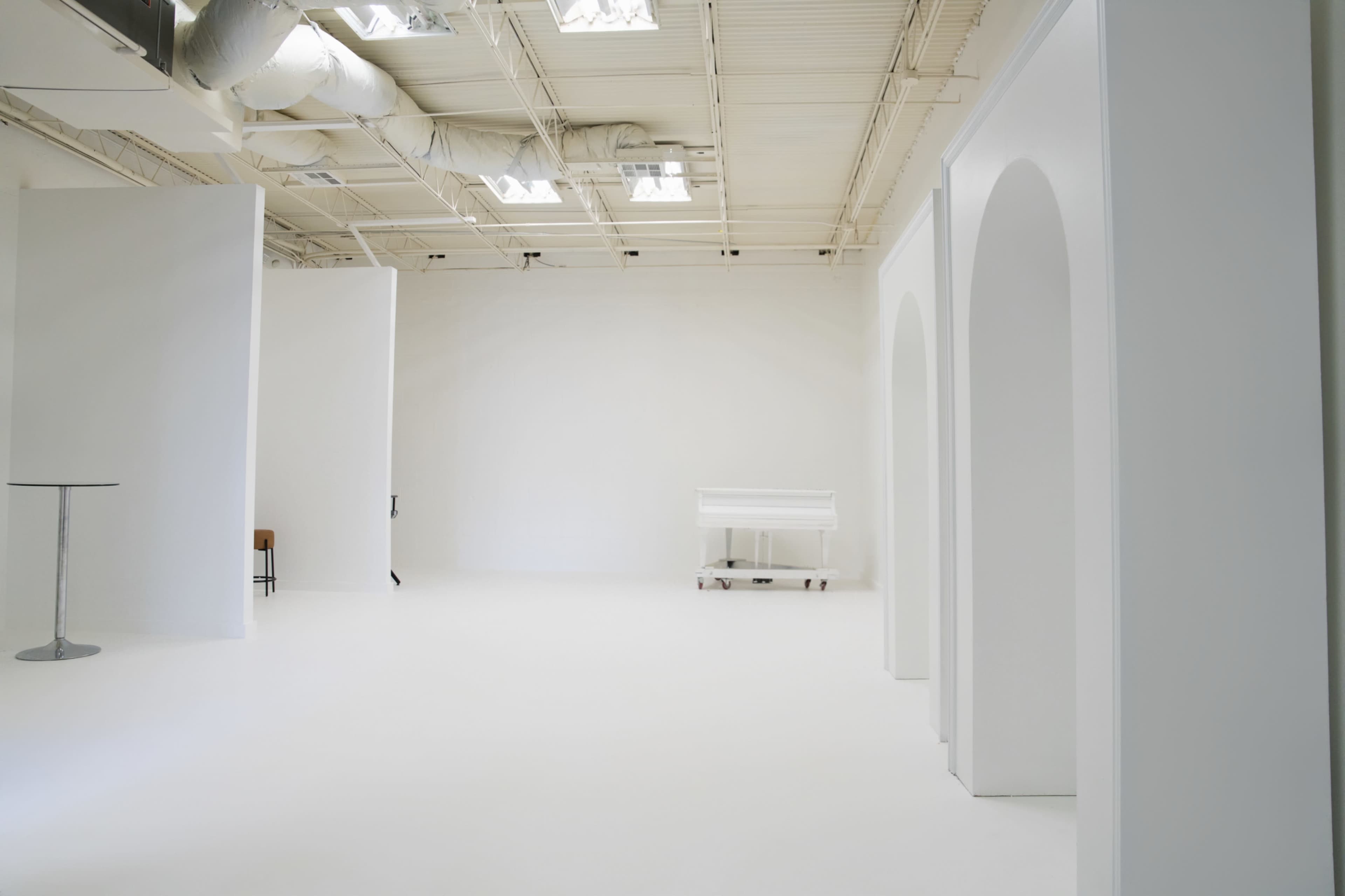 The image shows a spacious studio interior with white walls, a white floor, and several white archway structures.