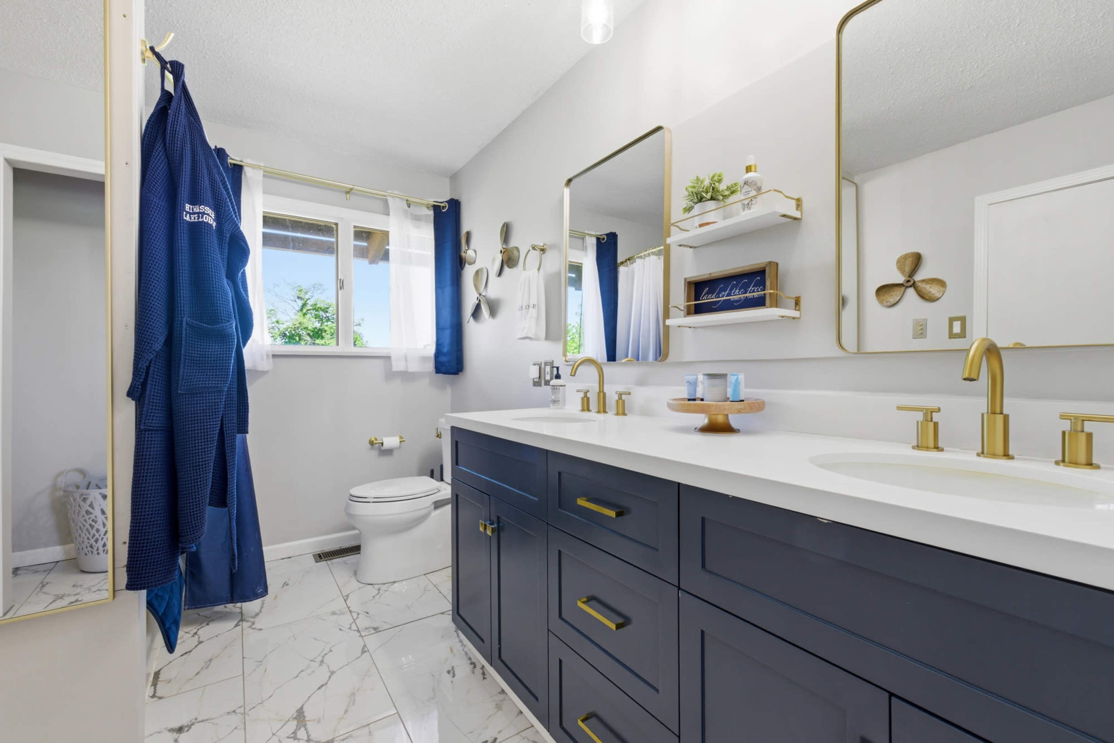 The image shows a modern bathroom with a double sink vanity, gold fixtures, a large mirror, and a combination of blue and white decor.