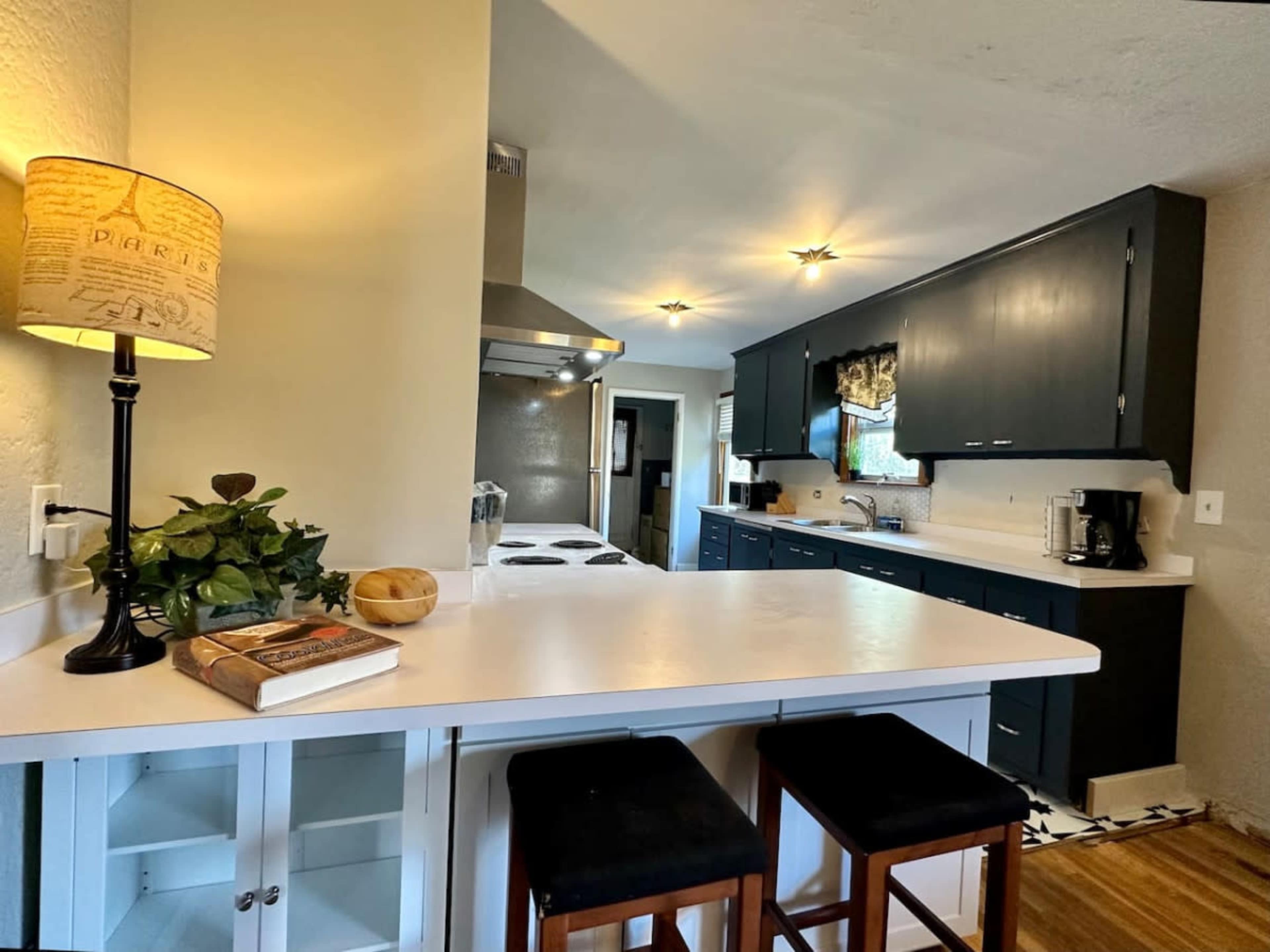 A modern kitchen features dark cabinetry, a stainless steel range hood, and a breakfast bar with two stools.