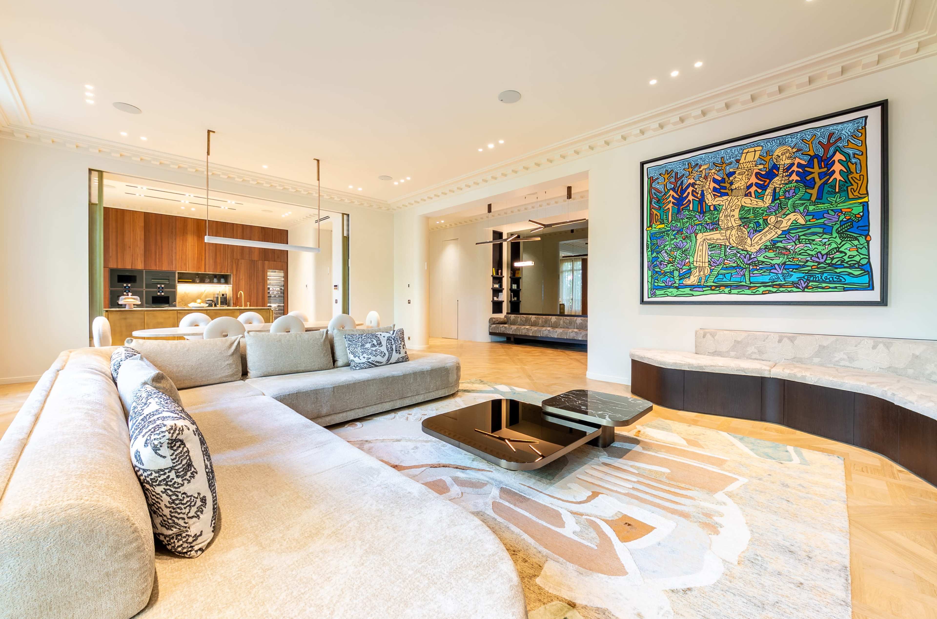 The image shows a spacious, modern living room with a large sectional sofa, a marble coffee table, and a colorful artwork on the wall.