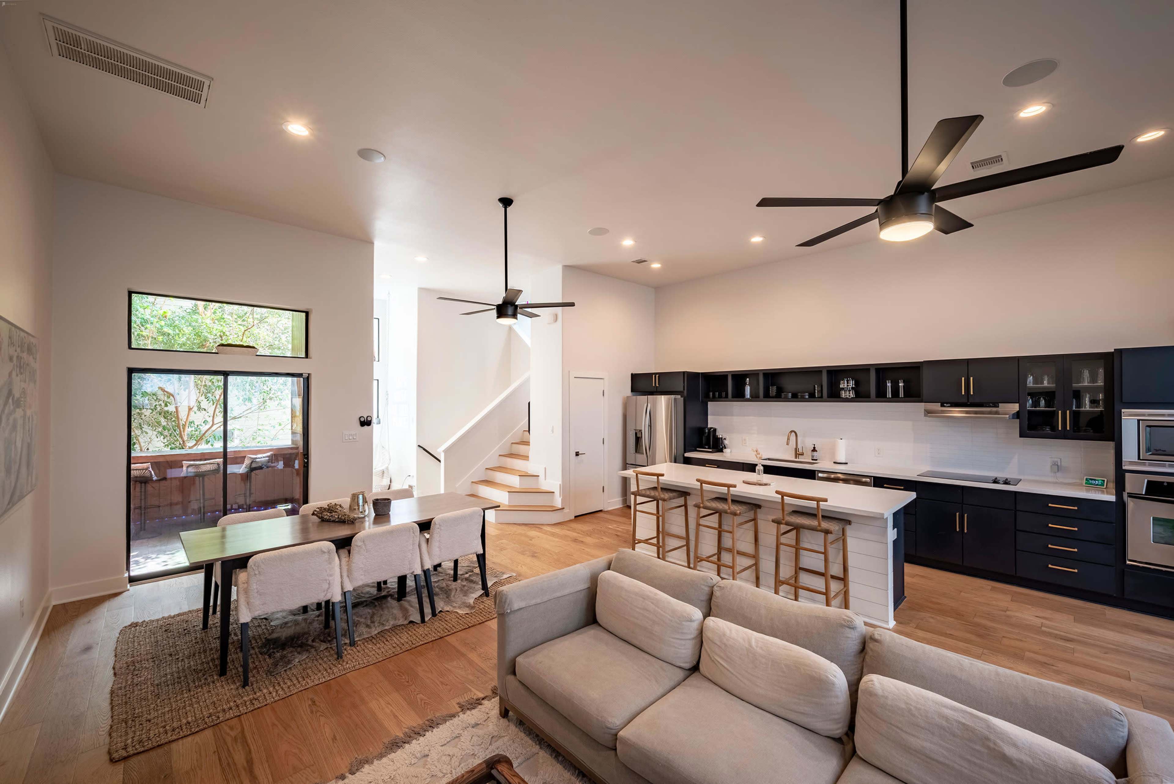 The image shows a modern open-concept living space featuring a kitchen, dining area, and seating area with a staircase in the background.