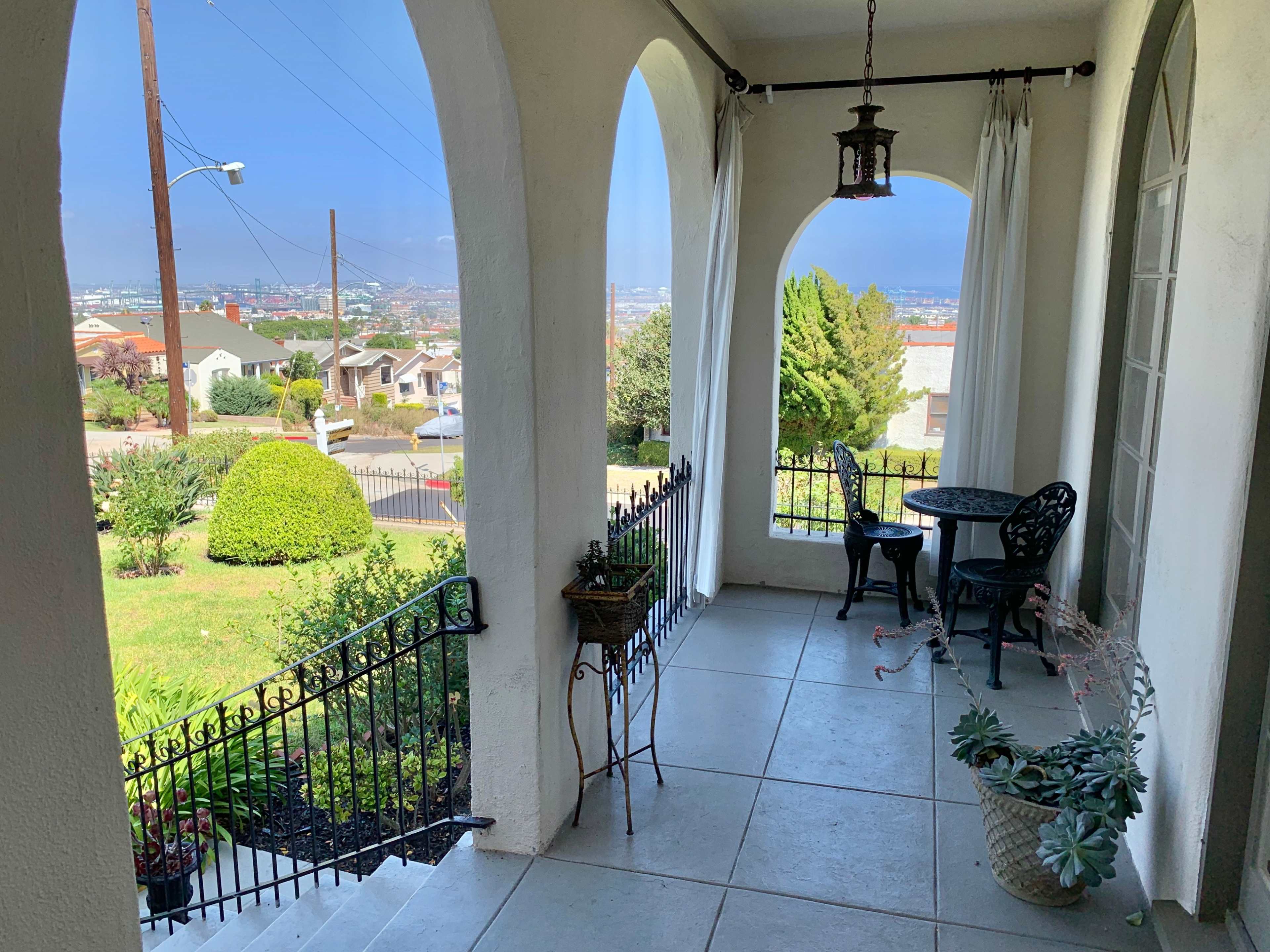 A spacious porch features arched openings, a small table and chairs, and a view of a suburban landscape.