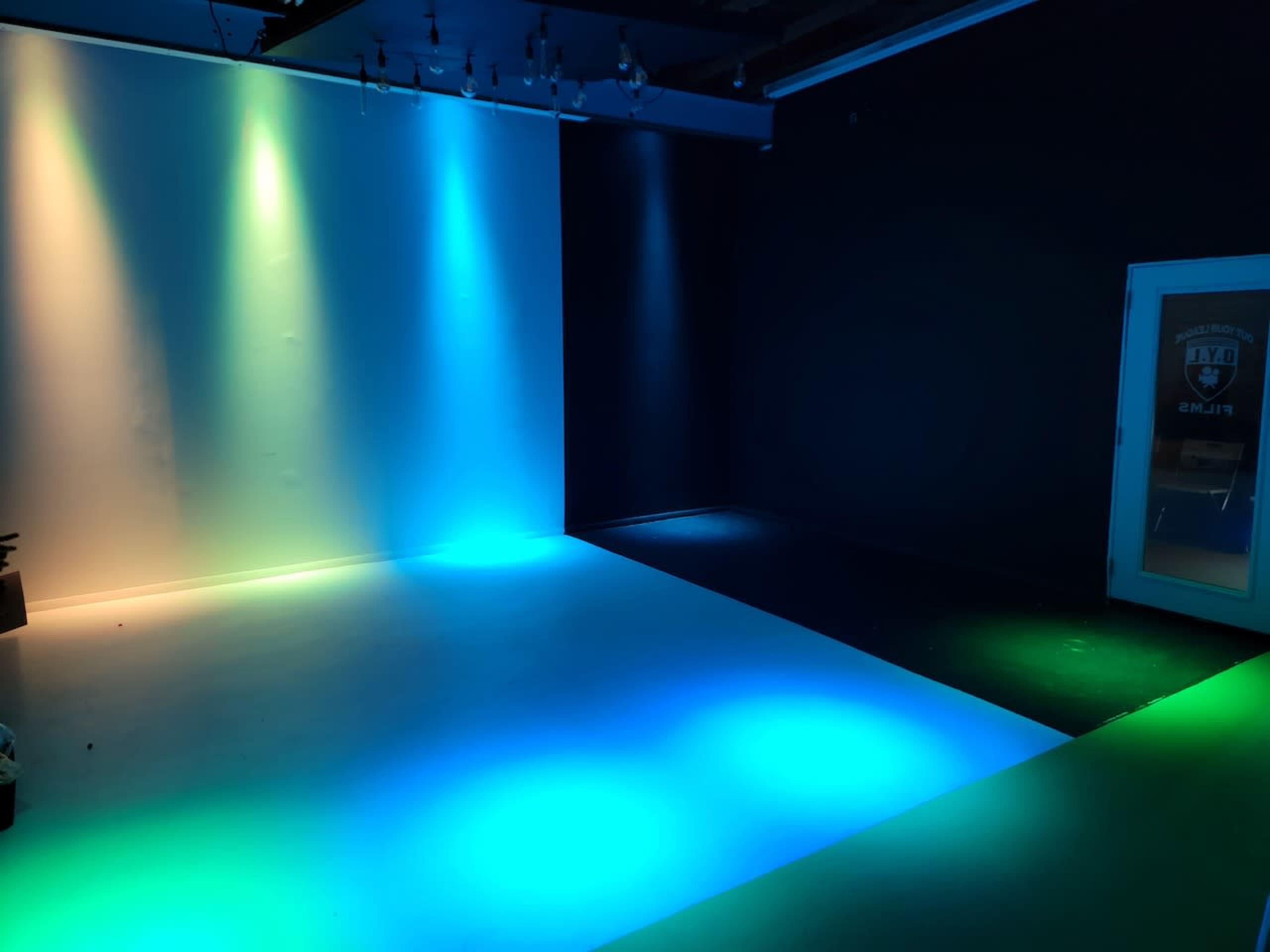 The image shows a studio space with colored lighting casting blue, green, and white hues on the floor and walls.
