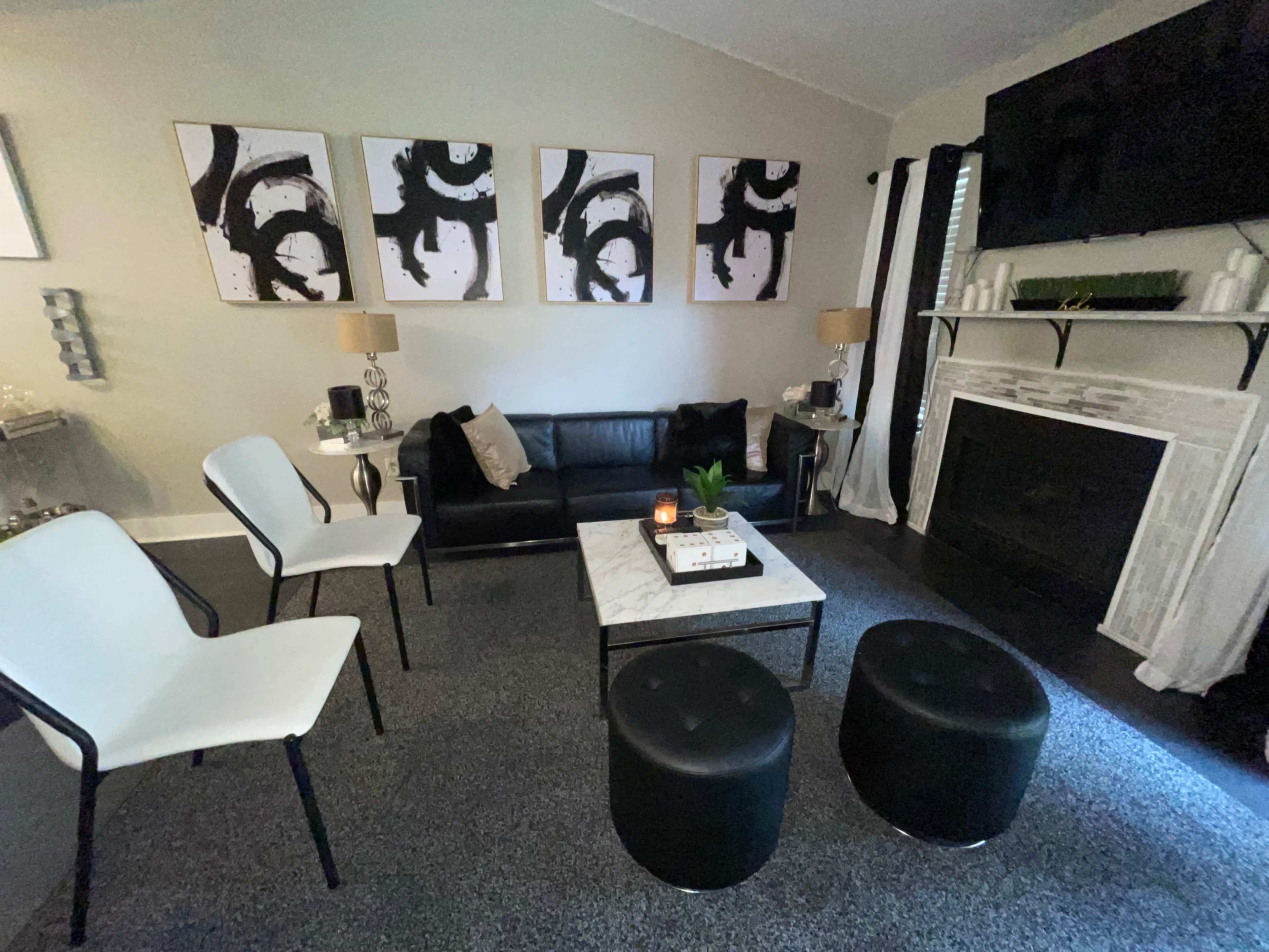 The living room features a black sofa, a marble coffee table, four chairs, and abstract wall art above the fireplace.