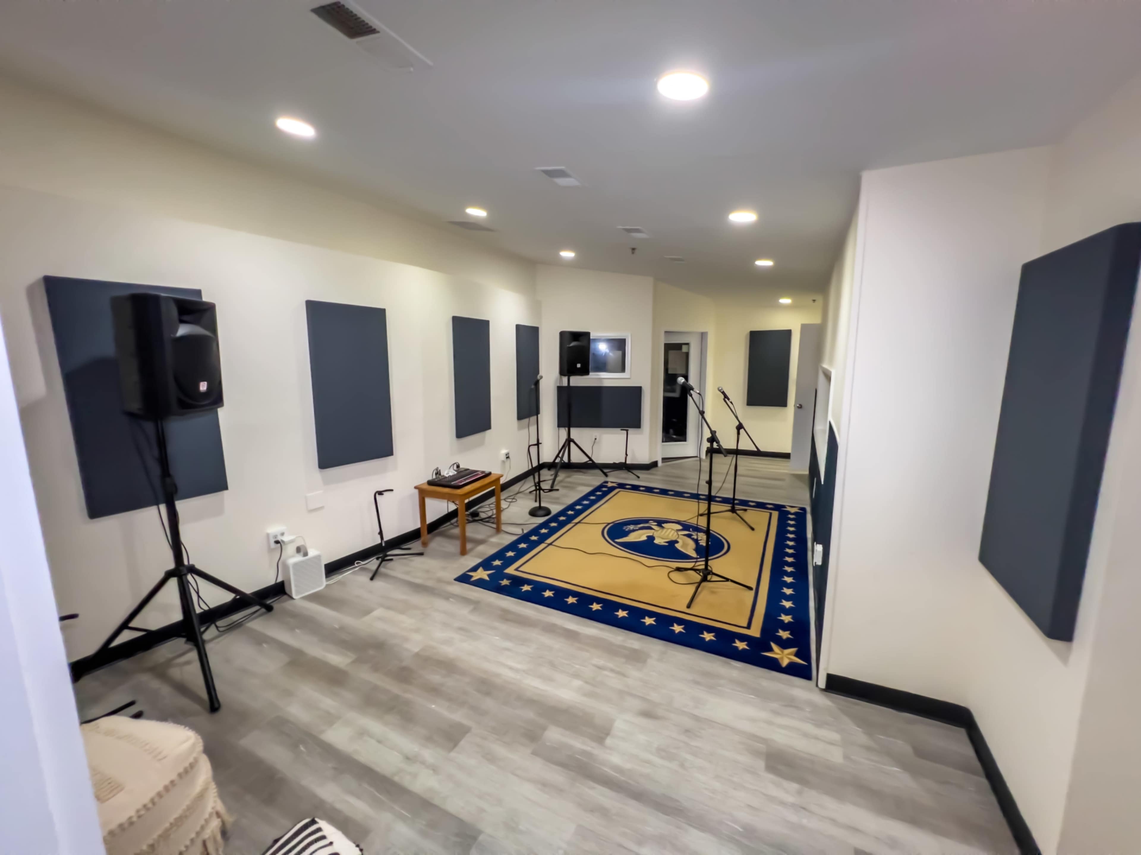 A soundproof recording studio featuring acoustic panels, two microphones on stands, and a blue carpet with a gold emblem.