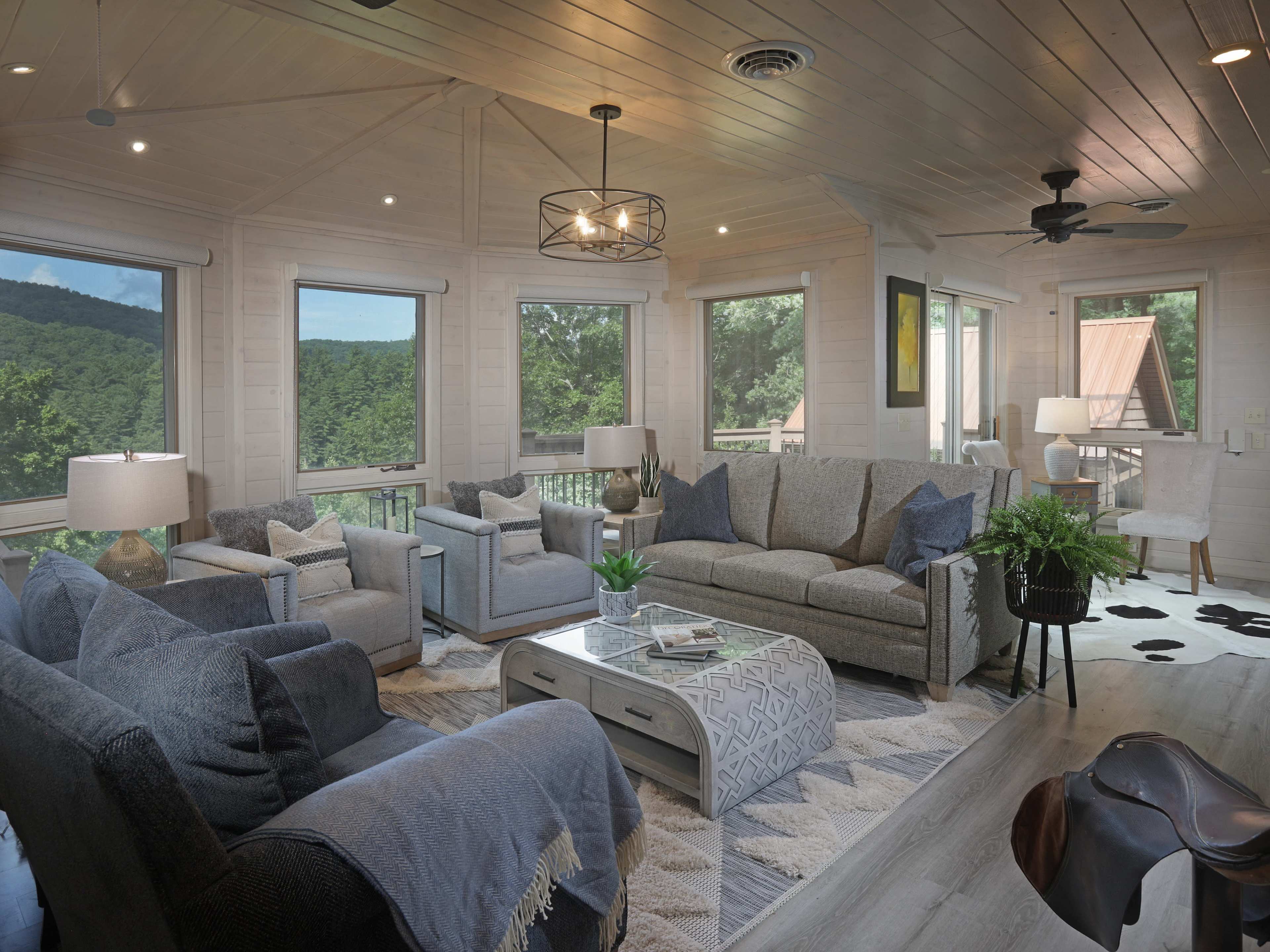 A bright and airy living room with large windows overlooking a mountain view, featuring gray sofas, a coffee table, and modern decor.