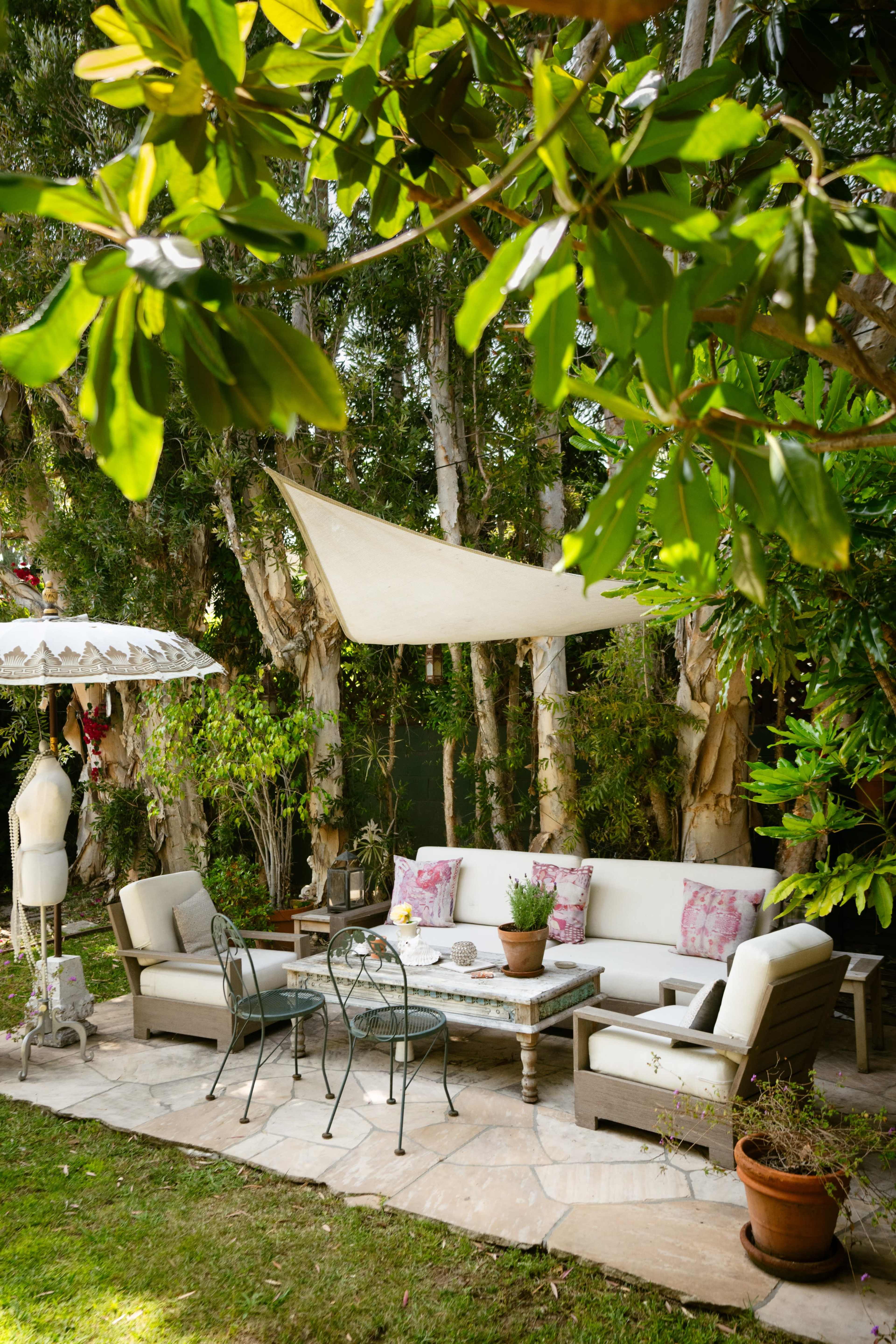 A cozy outdoor seating area is set up with cushioned chairs and a table surrounded by trees and potted plants.