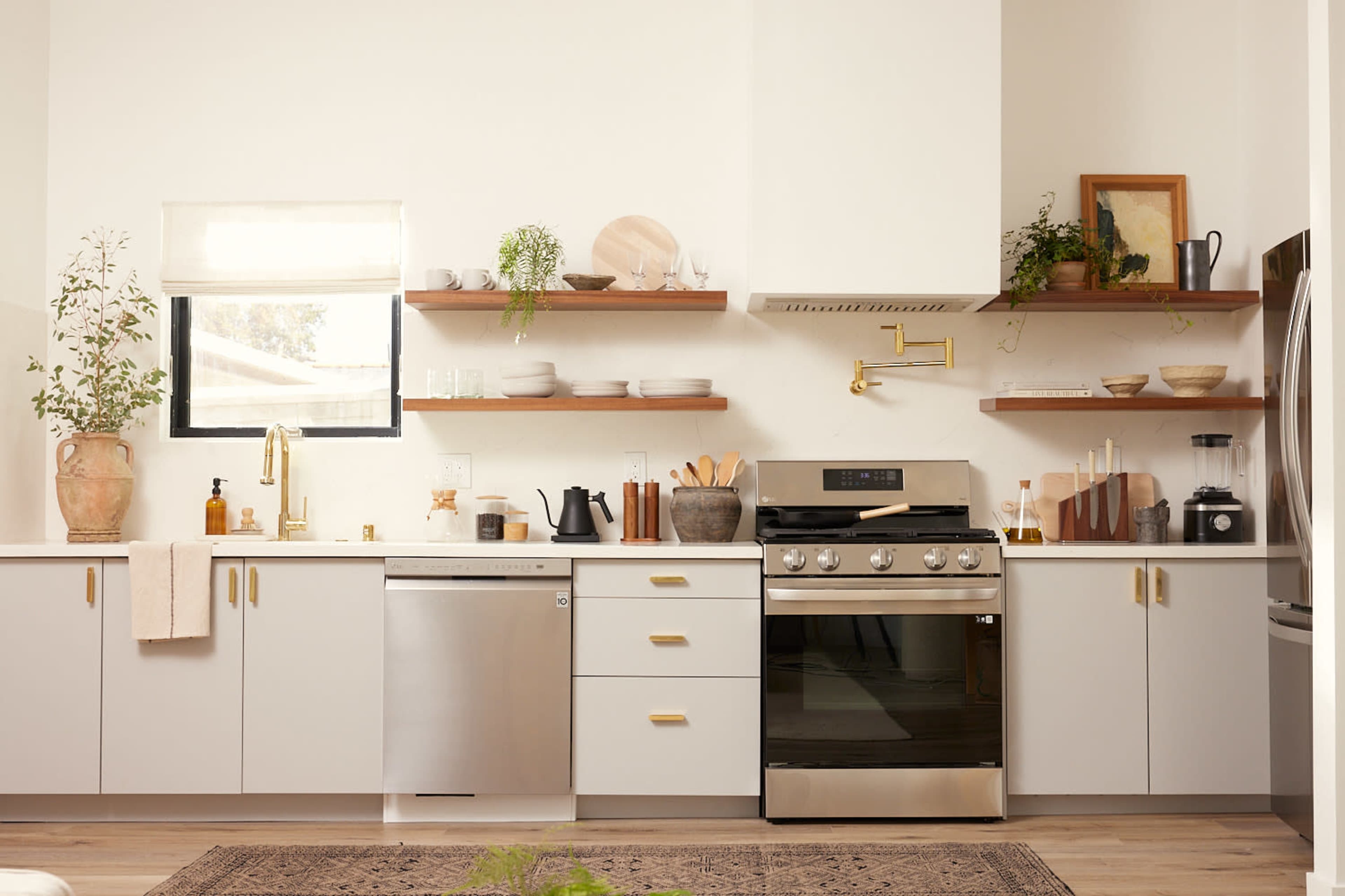 A modern kitchen features a stainless steel refrigerator, black stove, and open shelves displaying dishware and plants.