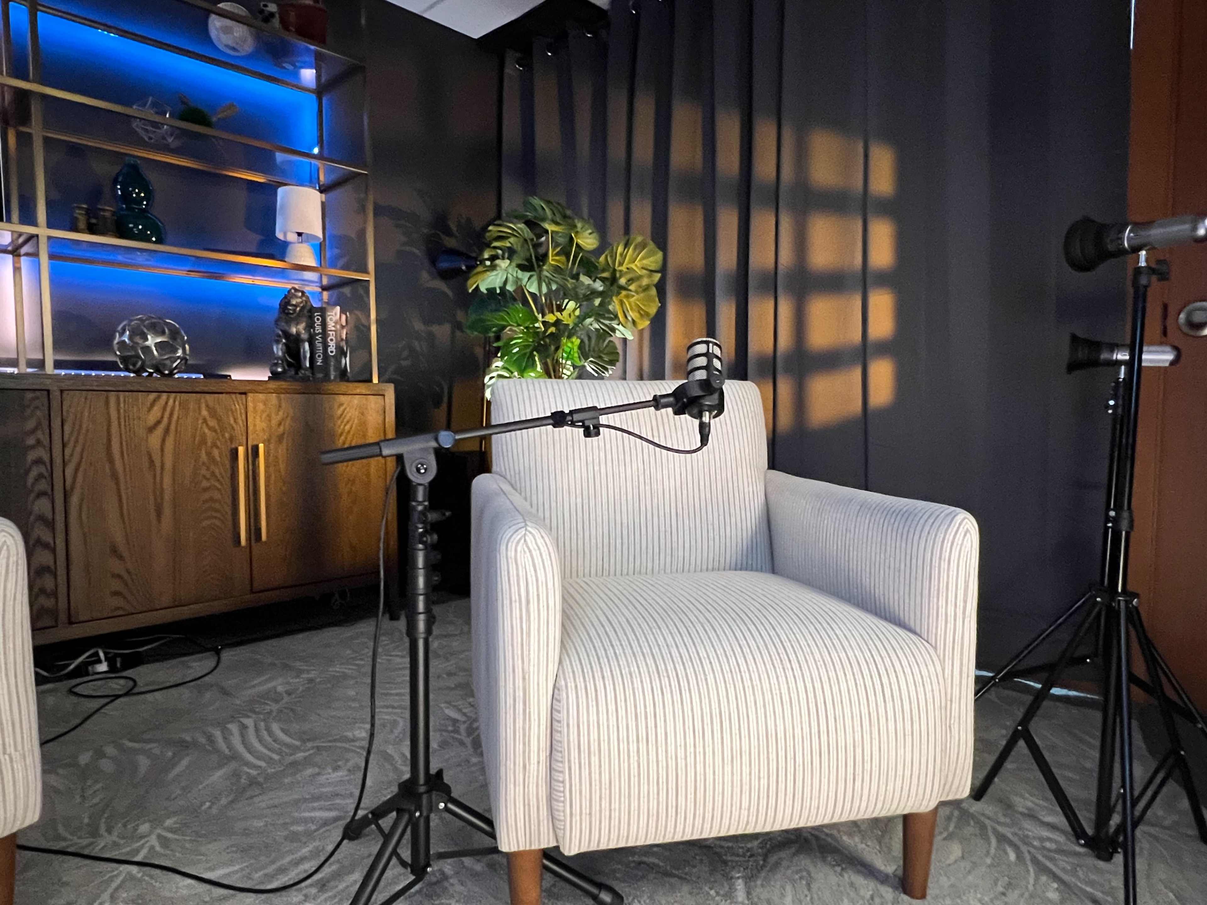 A light-colored armchair is positioned next to a microphone on a stand in a modern studio setting with dark curtains and stylized decor.