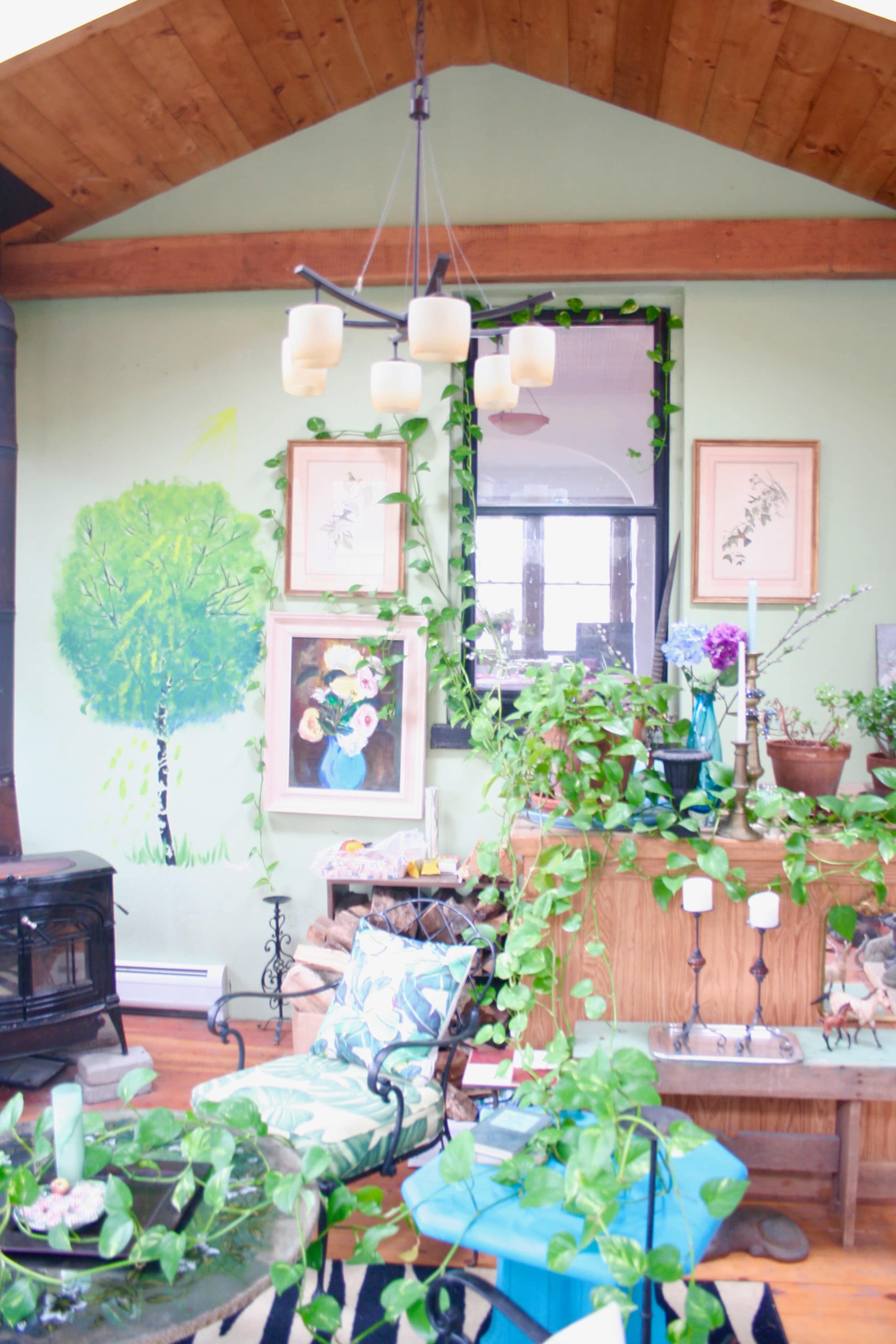 The room features a green wall adorned with plants, a chandelier, artwork, and a wooden table surrounded by chairs.