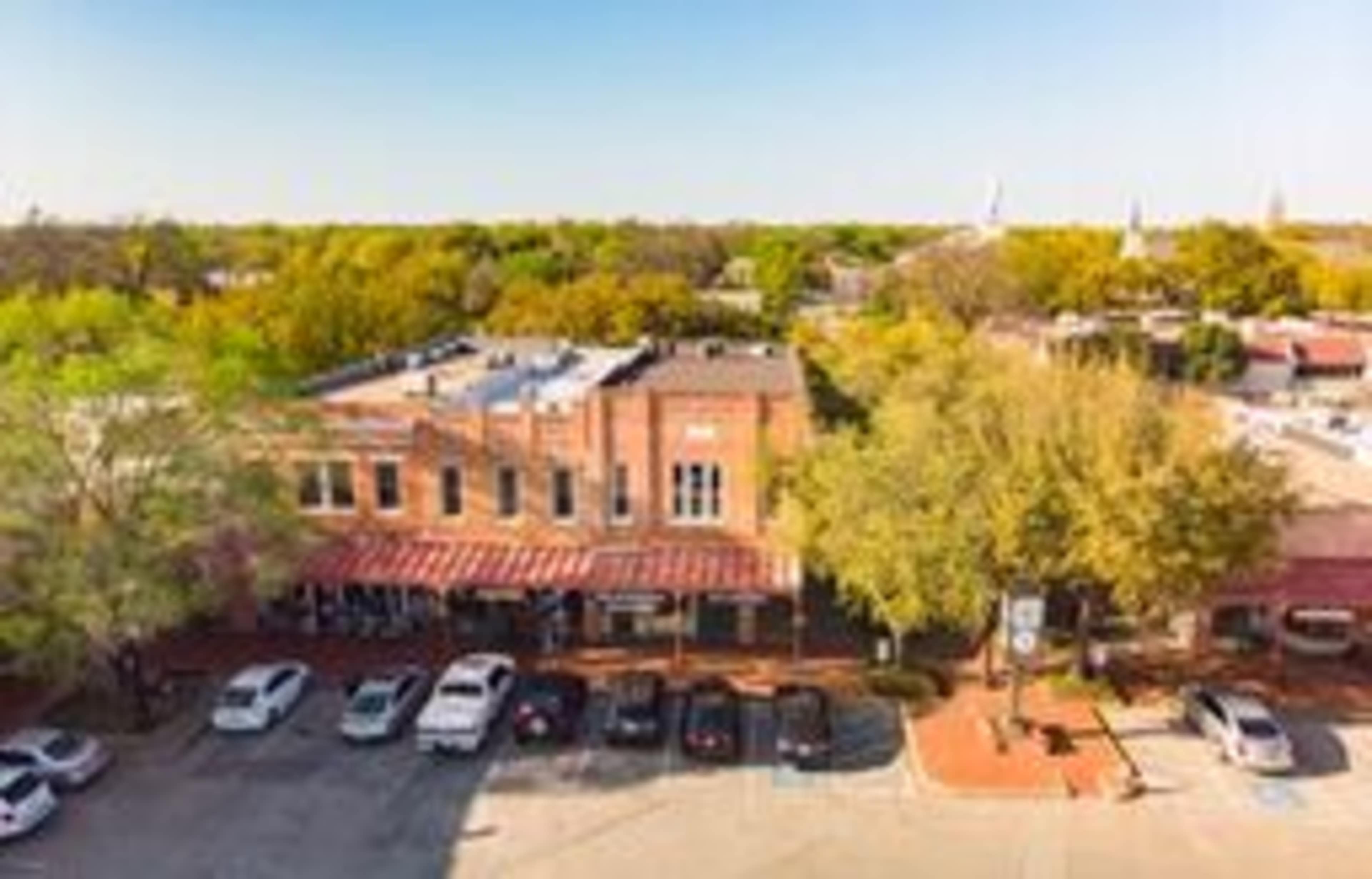 A red-brick building with a striped awning, situated near parked cars and surrounded by trees in a downtown area.