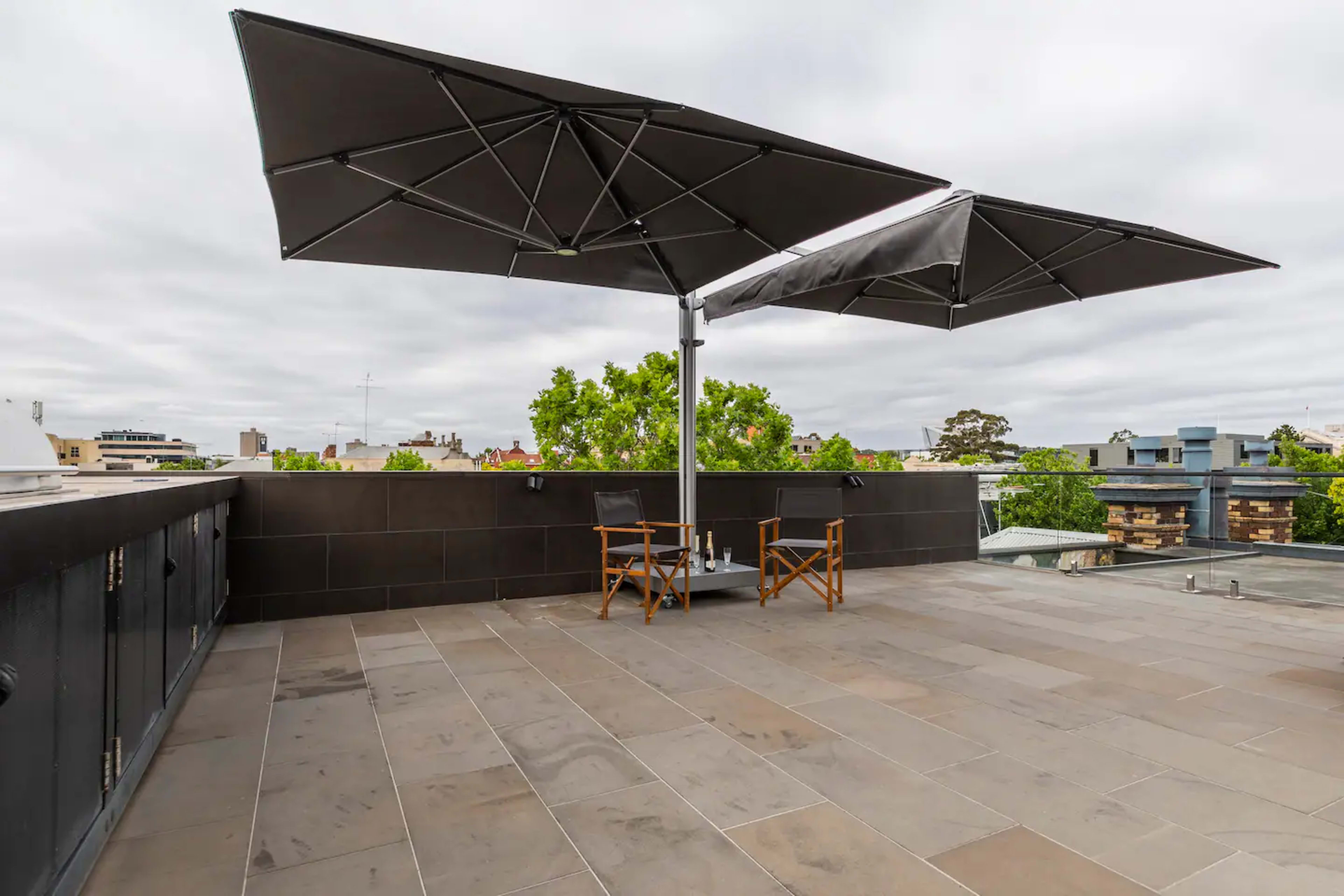 The image shows a rooftop terrace with two folding chairs and large umbrellas providing shade.
