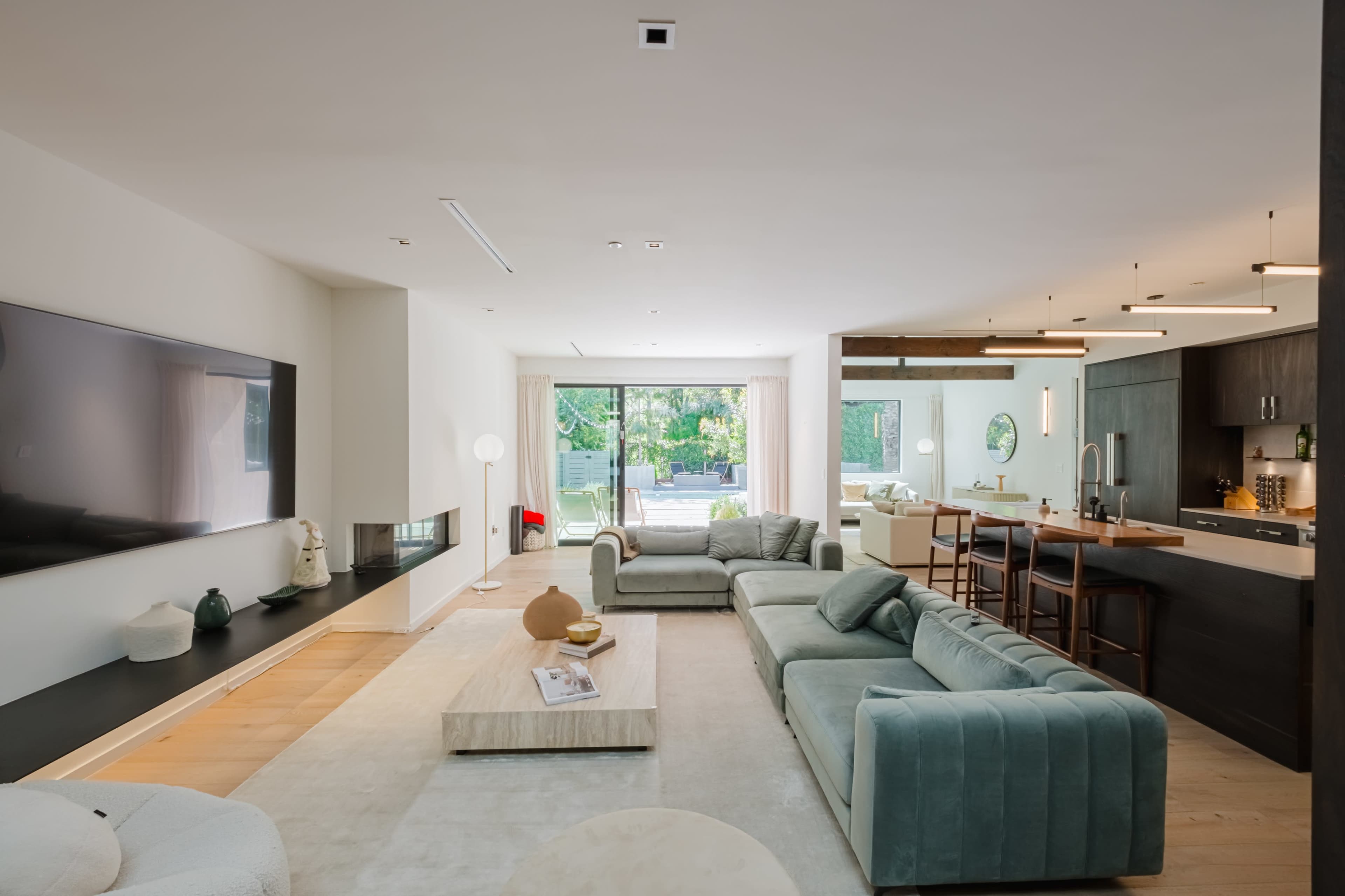 A modern living room with a sectional sofa, a coffee table, and a view of an open kitchen through large sliding glass doors.