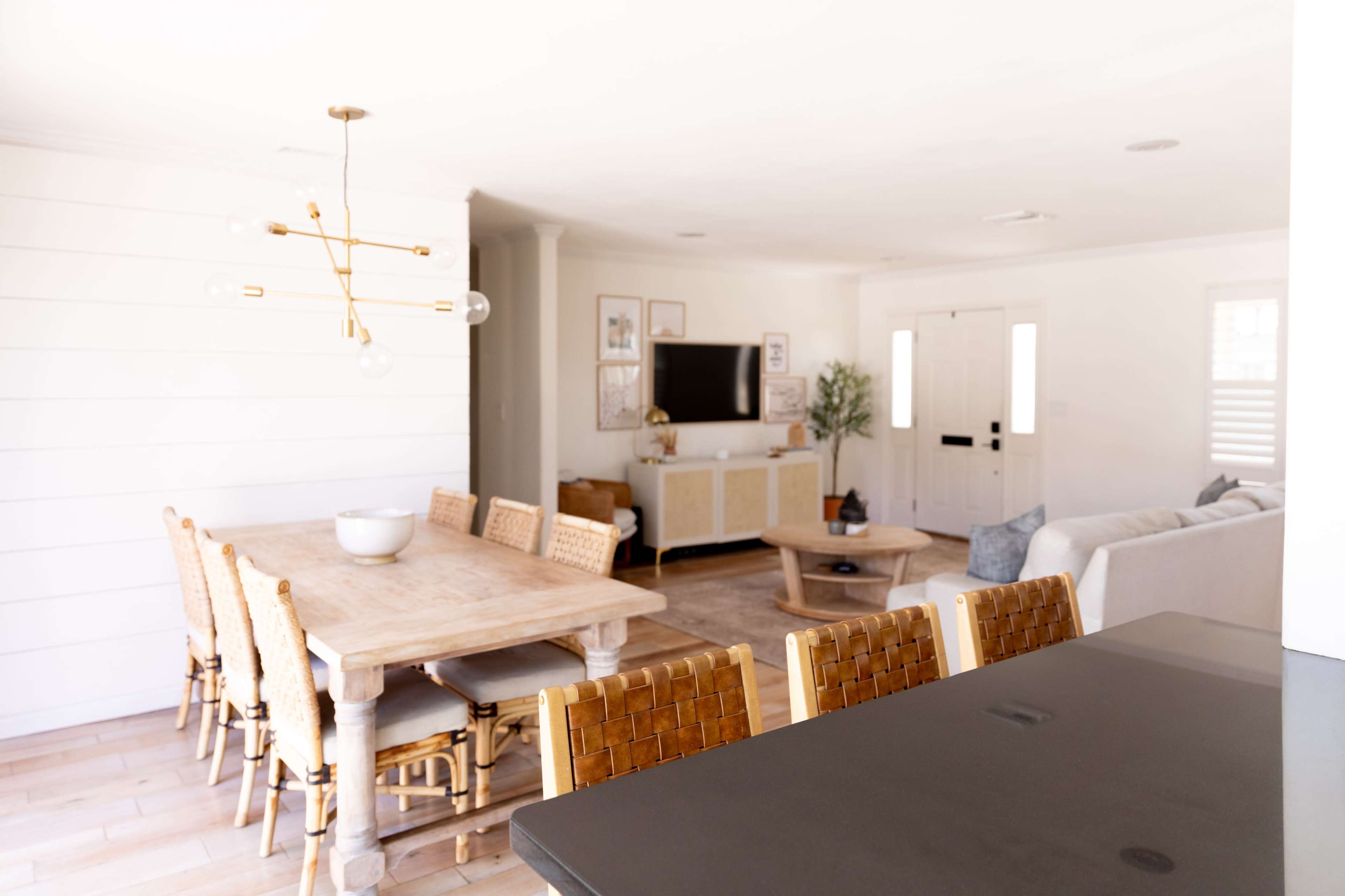 A dining area with a wooden table and woven chairs is situated adjacent to a living space featuring a television and a couch.