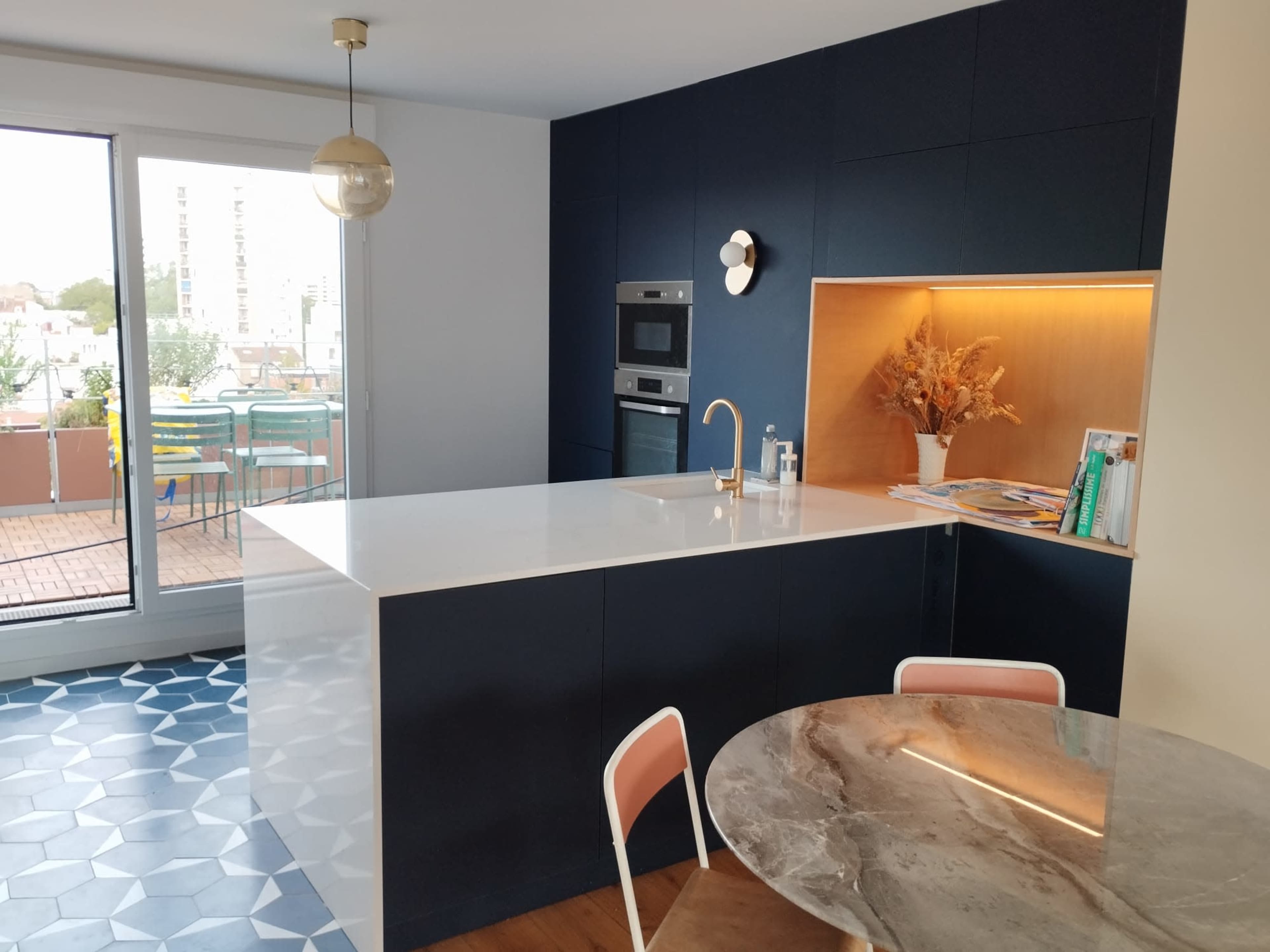 A modern kitchen featuring navy blue cabinetry, a white countertop, and a round marble dining table with pastel-colored chairs.