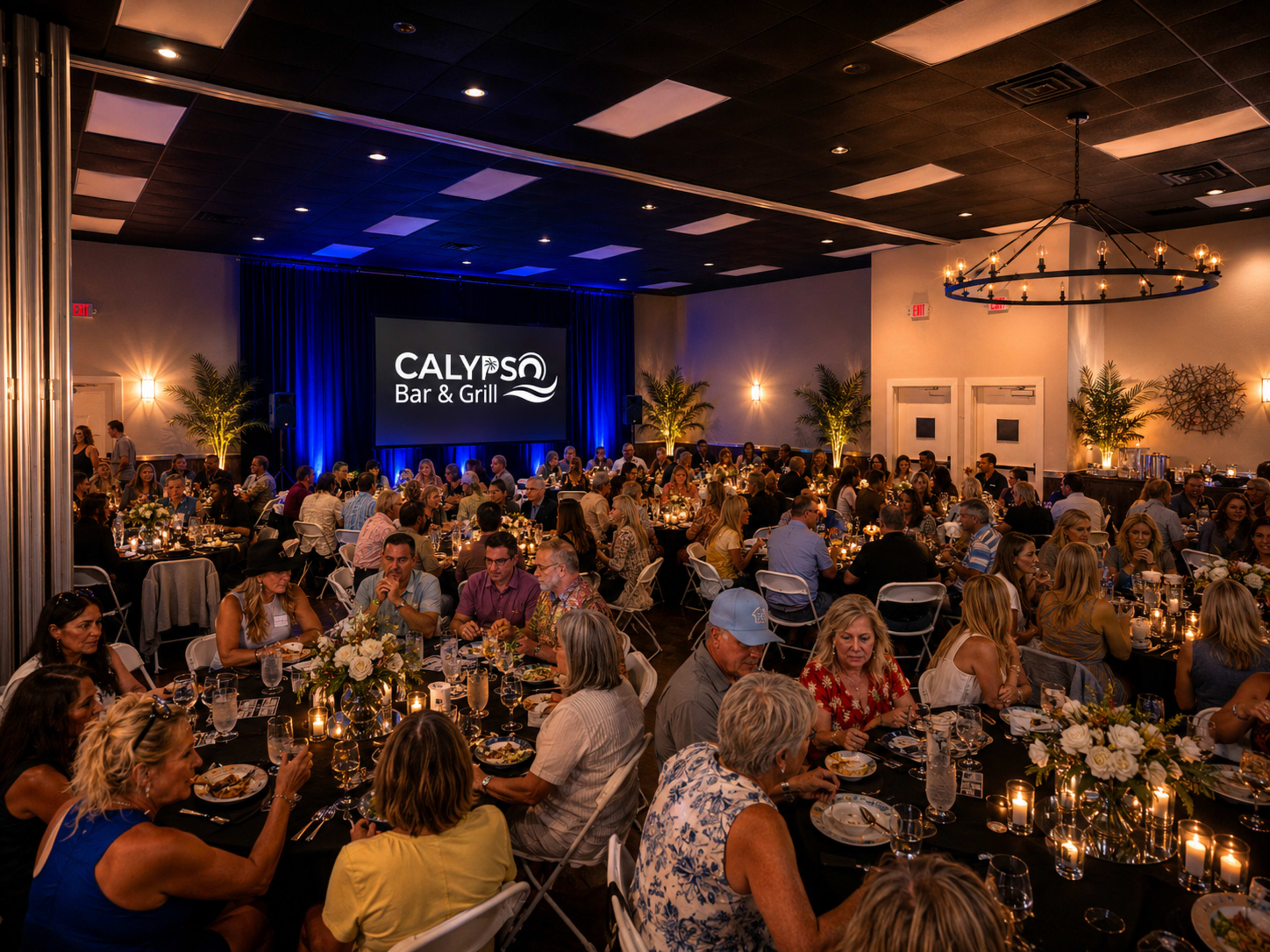 A large group of people dine at elegantly set tables in a well-lit banquet hall featuring a bar and grill theme.