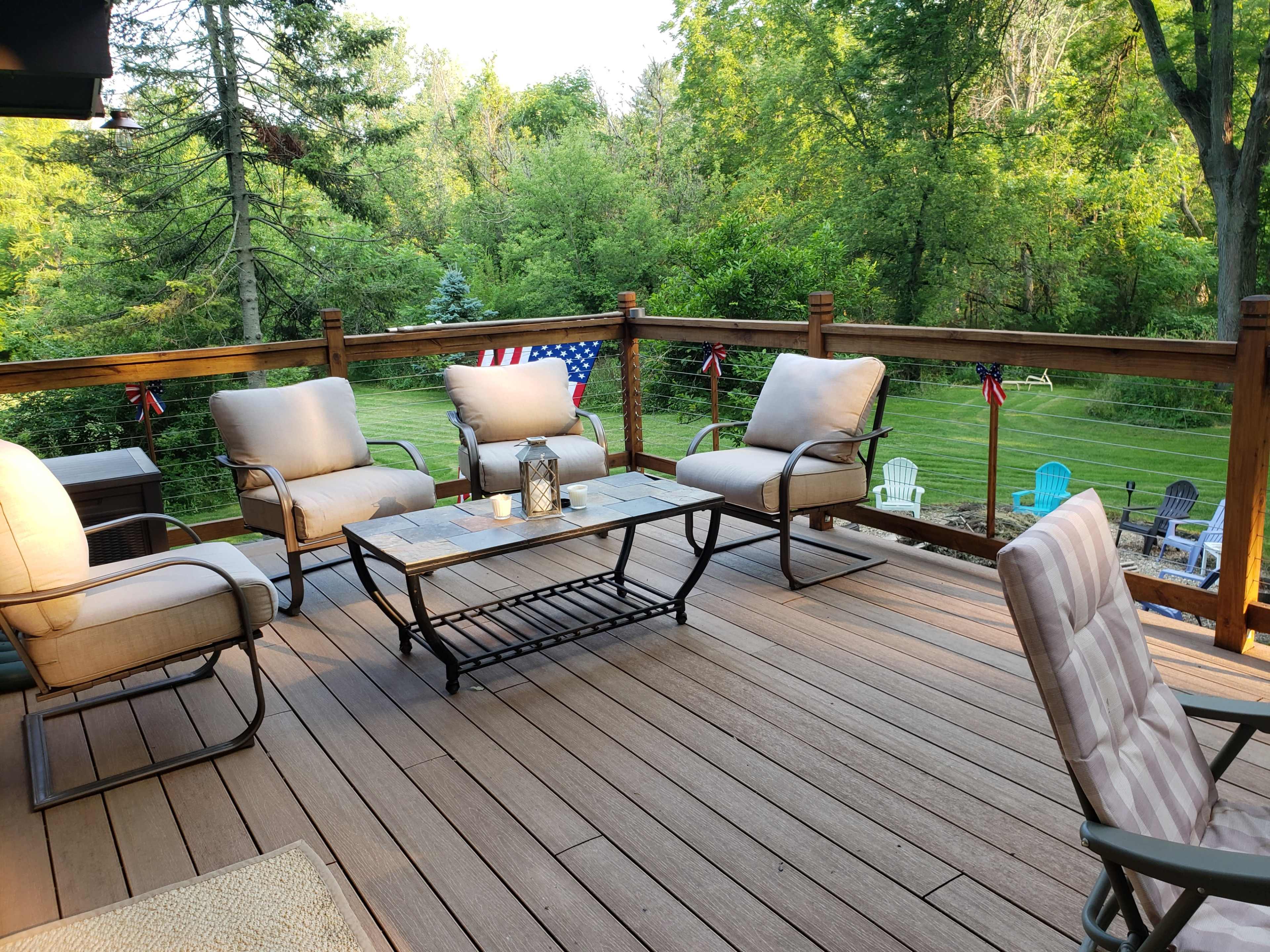 The image shows a deck area with several outdoor chairs and a table, surrounded by trees and lawn furniture in the background.