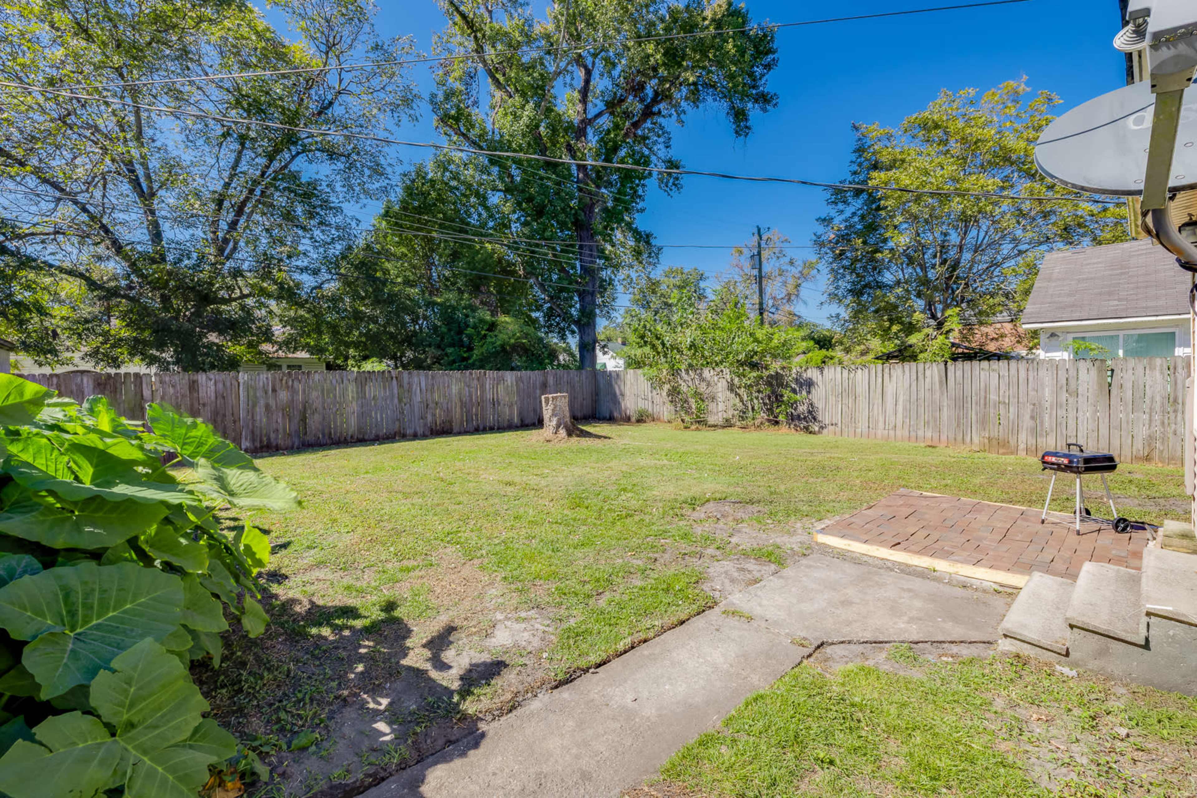 The image shows a fenced backyard with a tree stump and a small patio area featuring steps.
