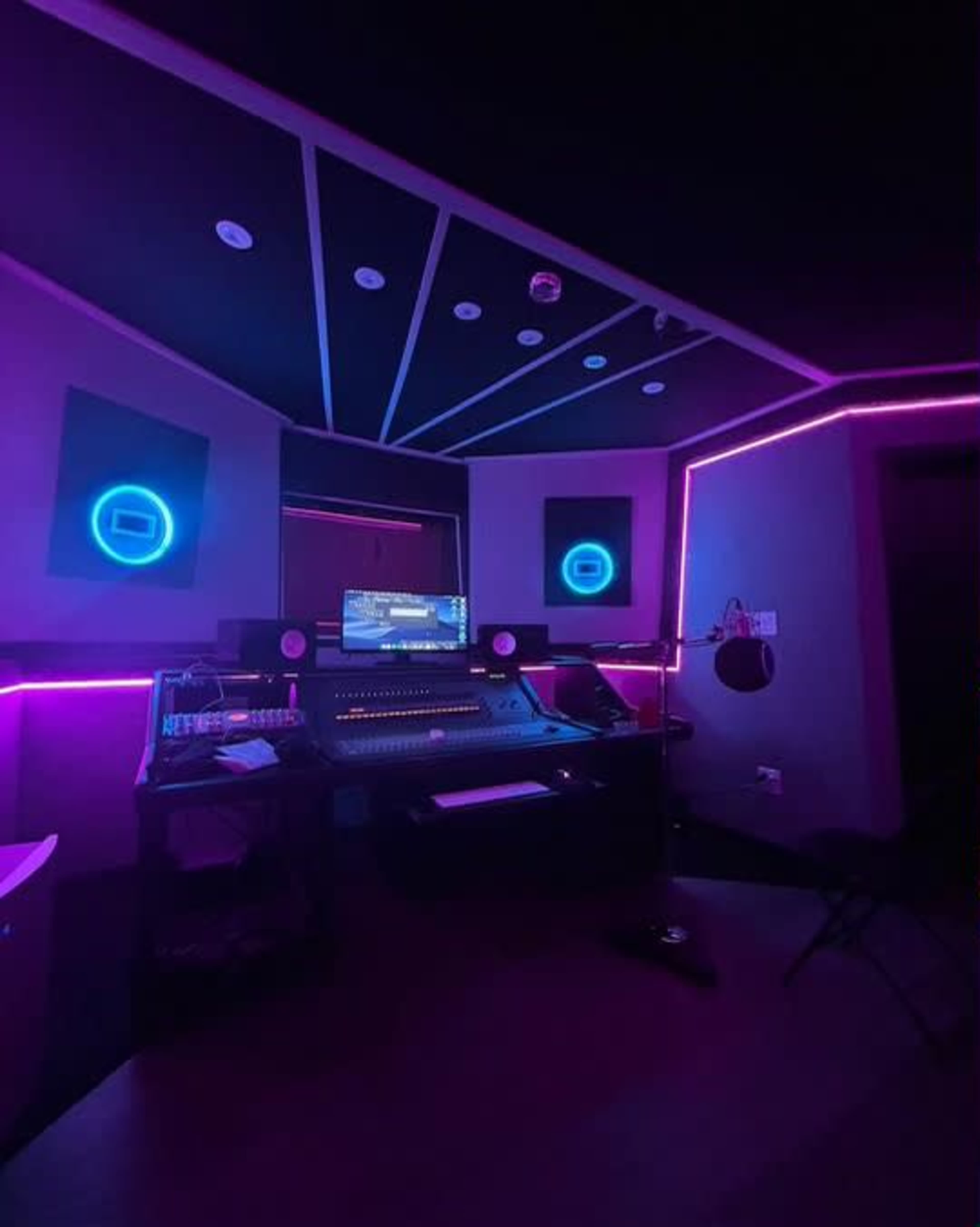 The image shows a music recording studio illuminated by neon lights with a digital mixing console and a computer setup.