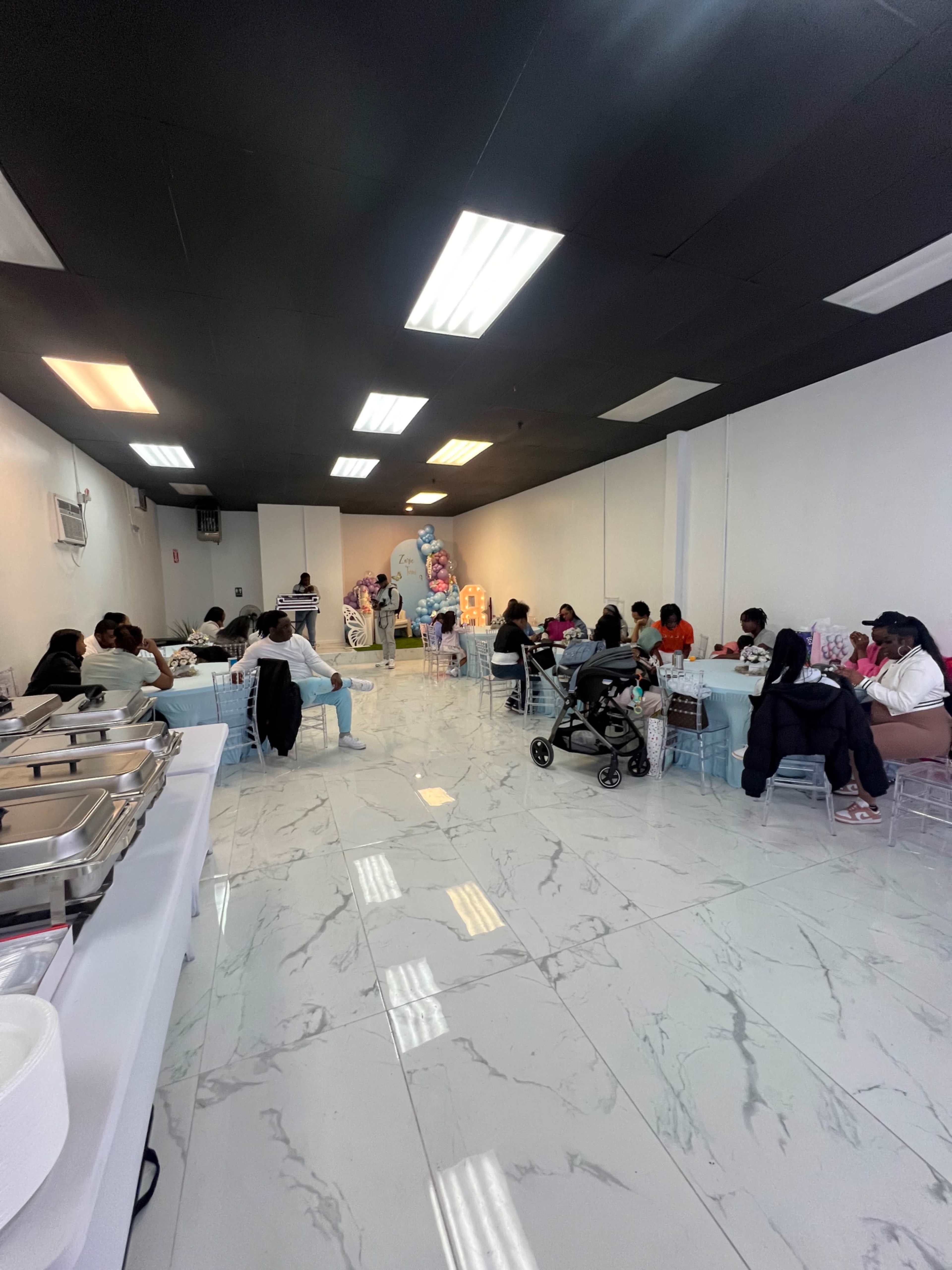 A spacious dining area with people seated at various tables while a buffet setup is visible on the left side.