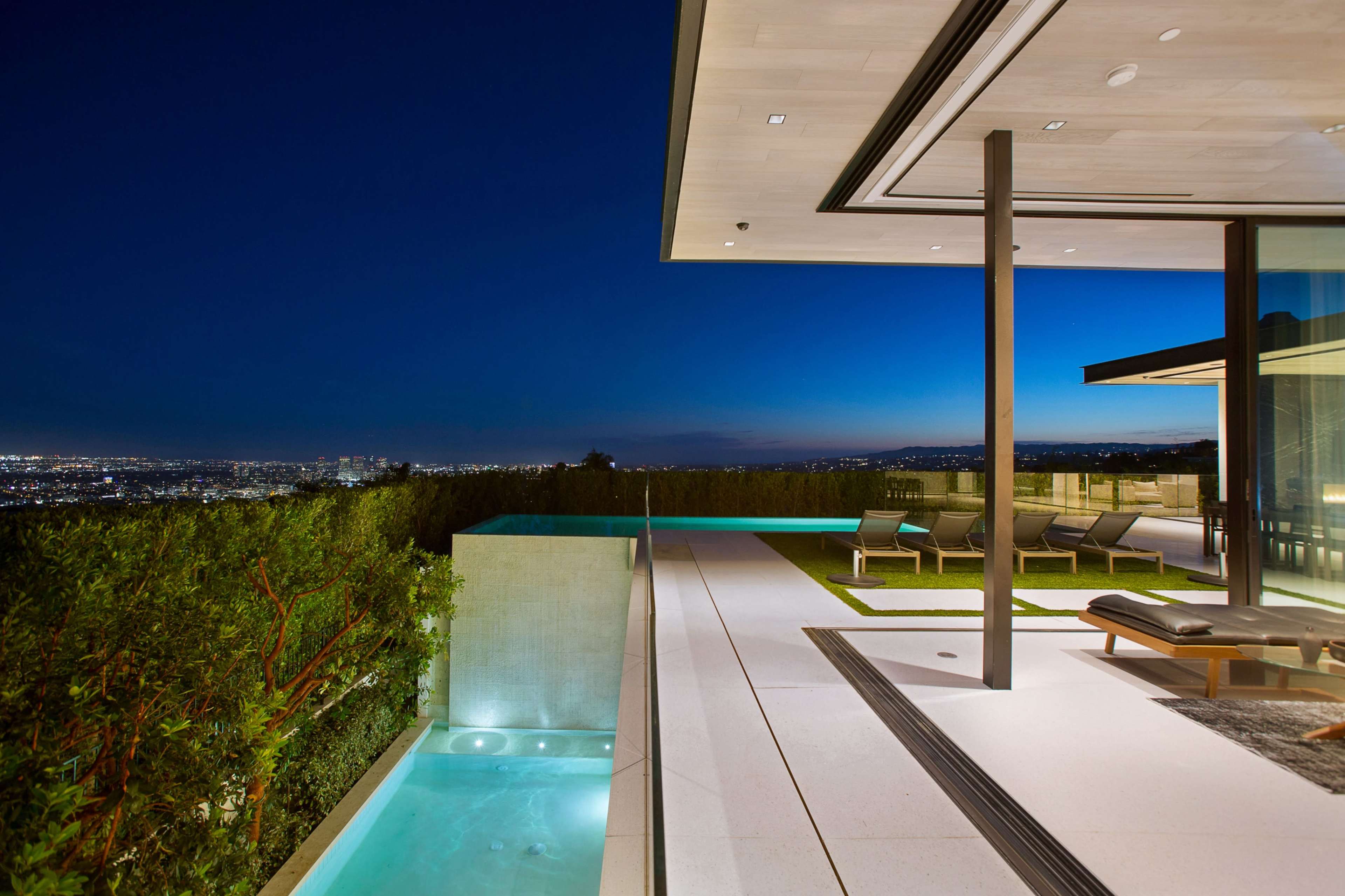This image shows a modern villa with a swimming pool and a view of the city skyline at night.